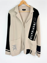 Beige cardigan with black sleeves on a hanger against a white background