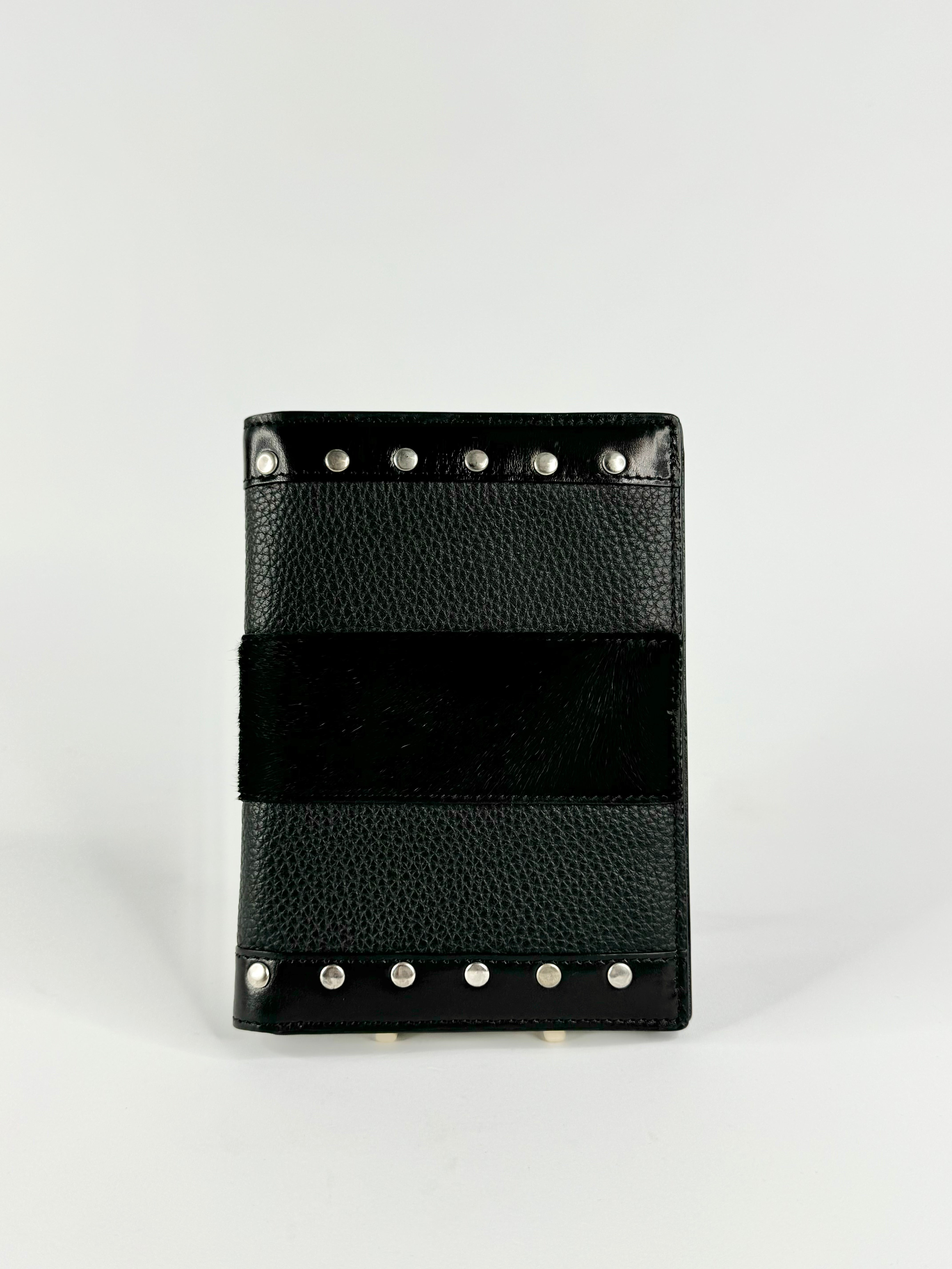 A black leather wallet with a textured pebbled finish, a wide black suede-like horizontal stripe across the center, and silver-tone metal studs along the top and bottom edges, shown on a light gray background.