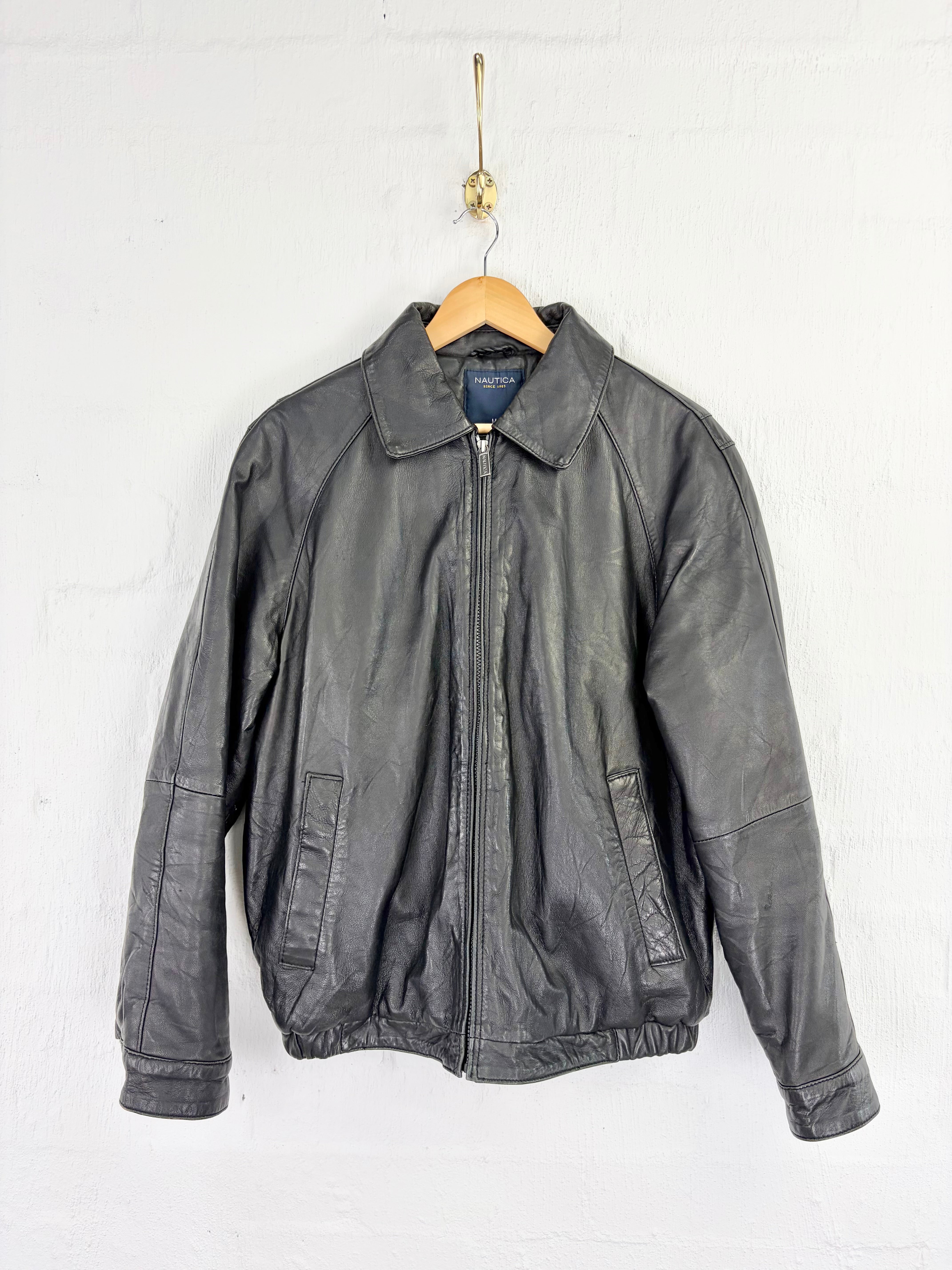 A dark gray leather jacket hanging on a wooden hanger against a white painted brick wall.