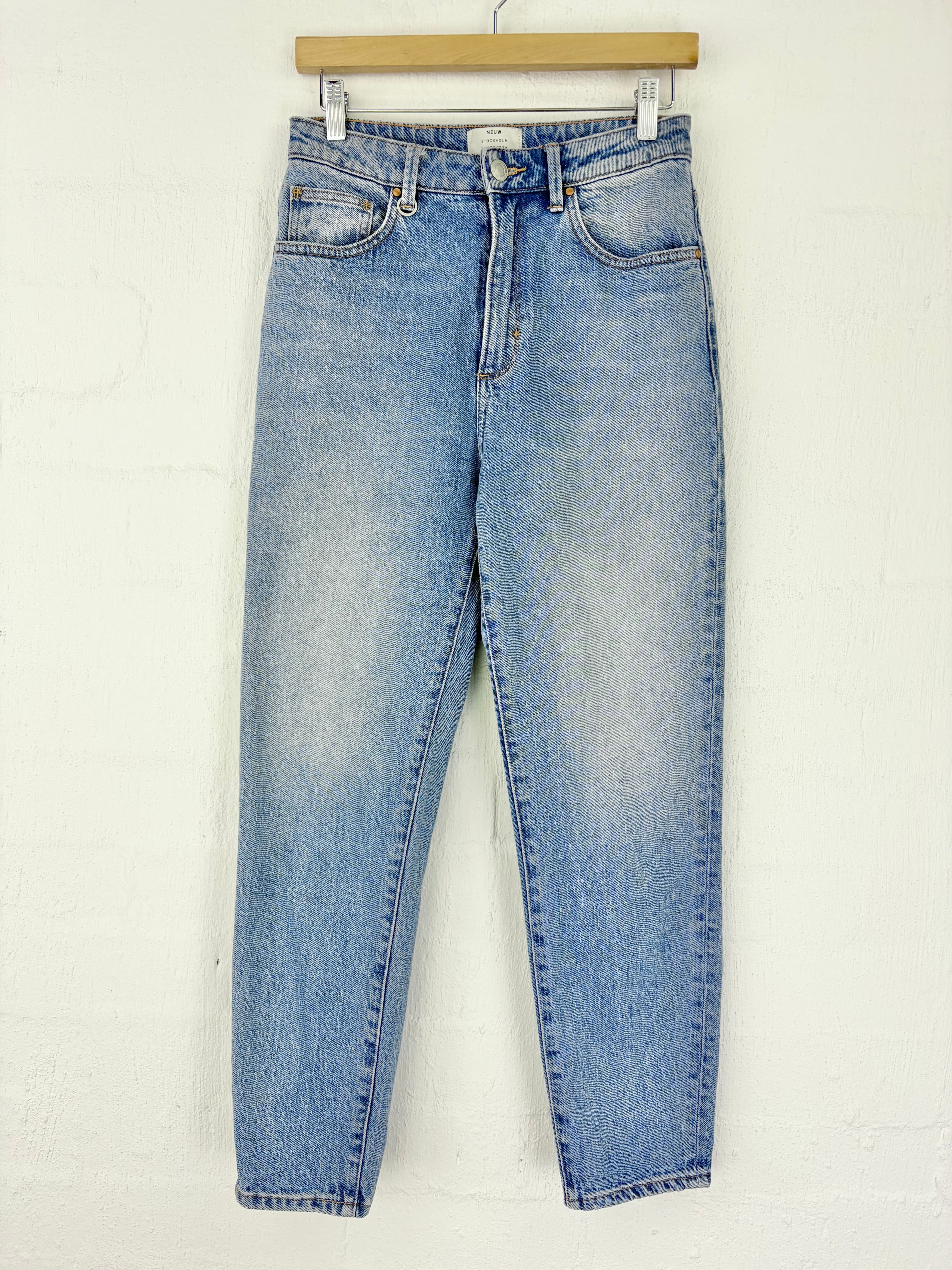 Light blue high-waisted skinny jeans hanging from a wooden hanger against a white textured wall.