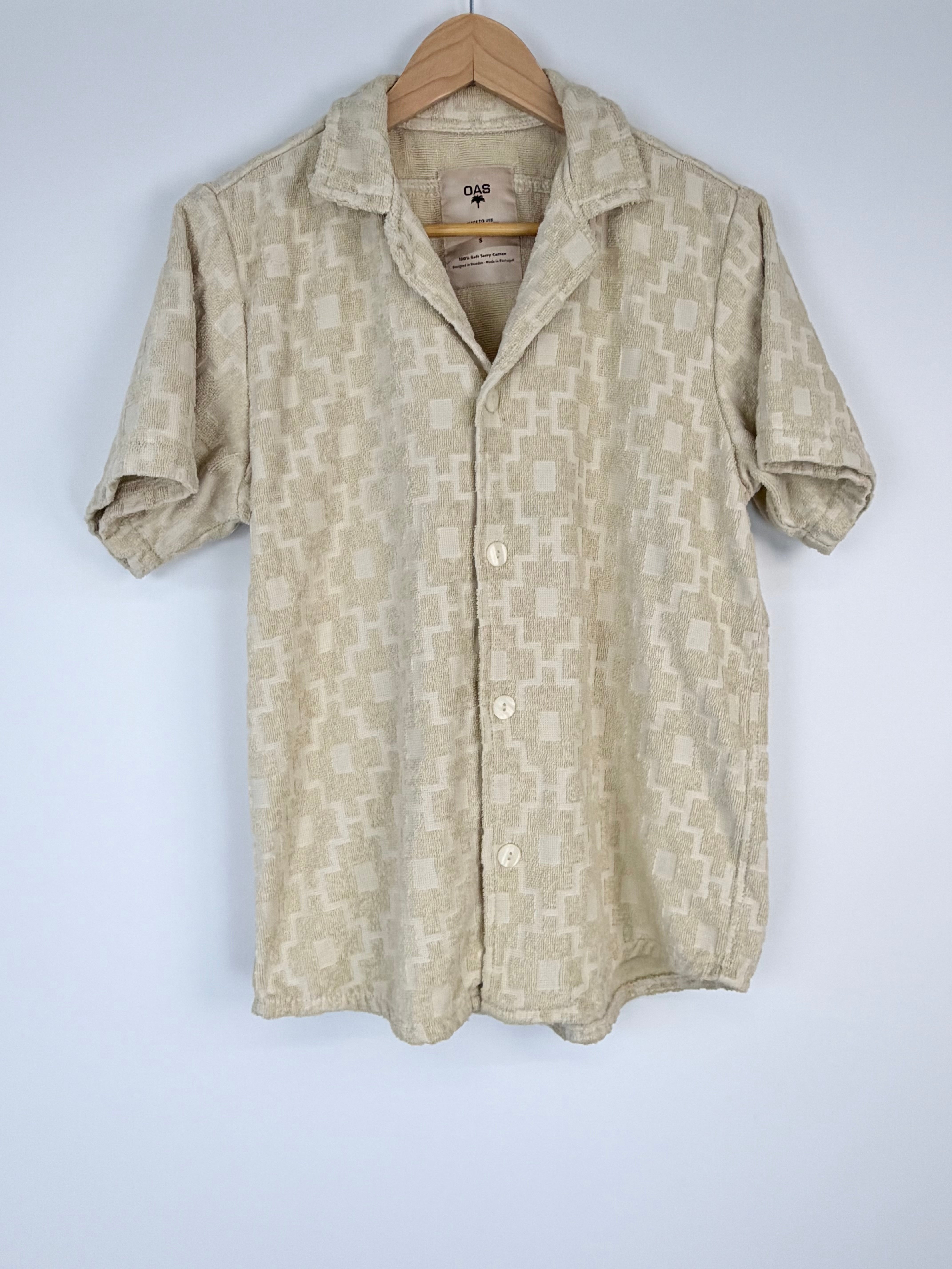 Beige patterned shirt on a hanger against a white background