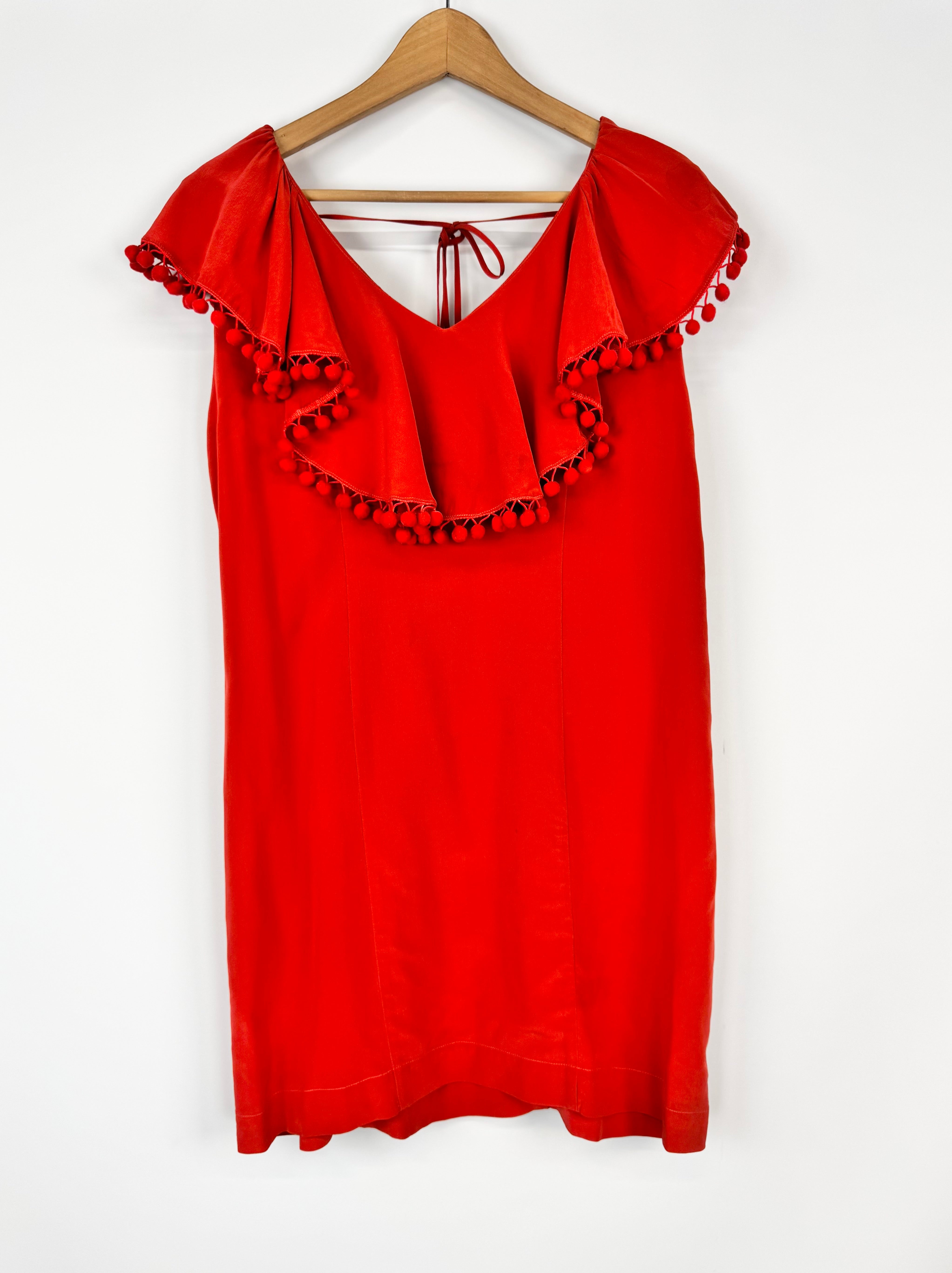 Red top with pom-pom details on a wooden hanger against a white background