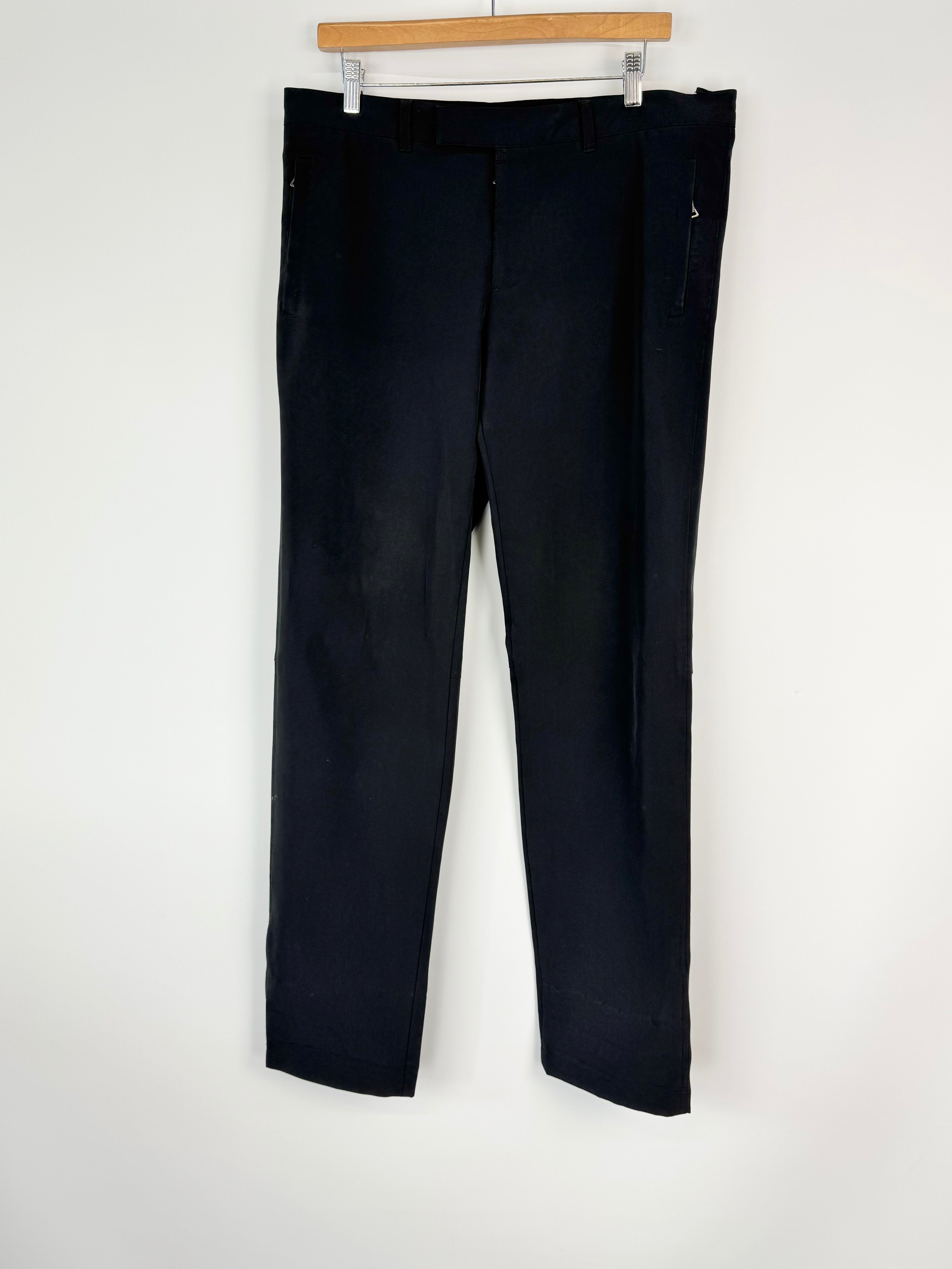 Black pants hanging on a wooden hanger against a white wall