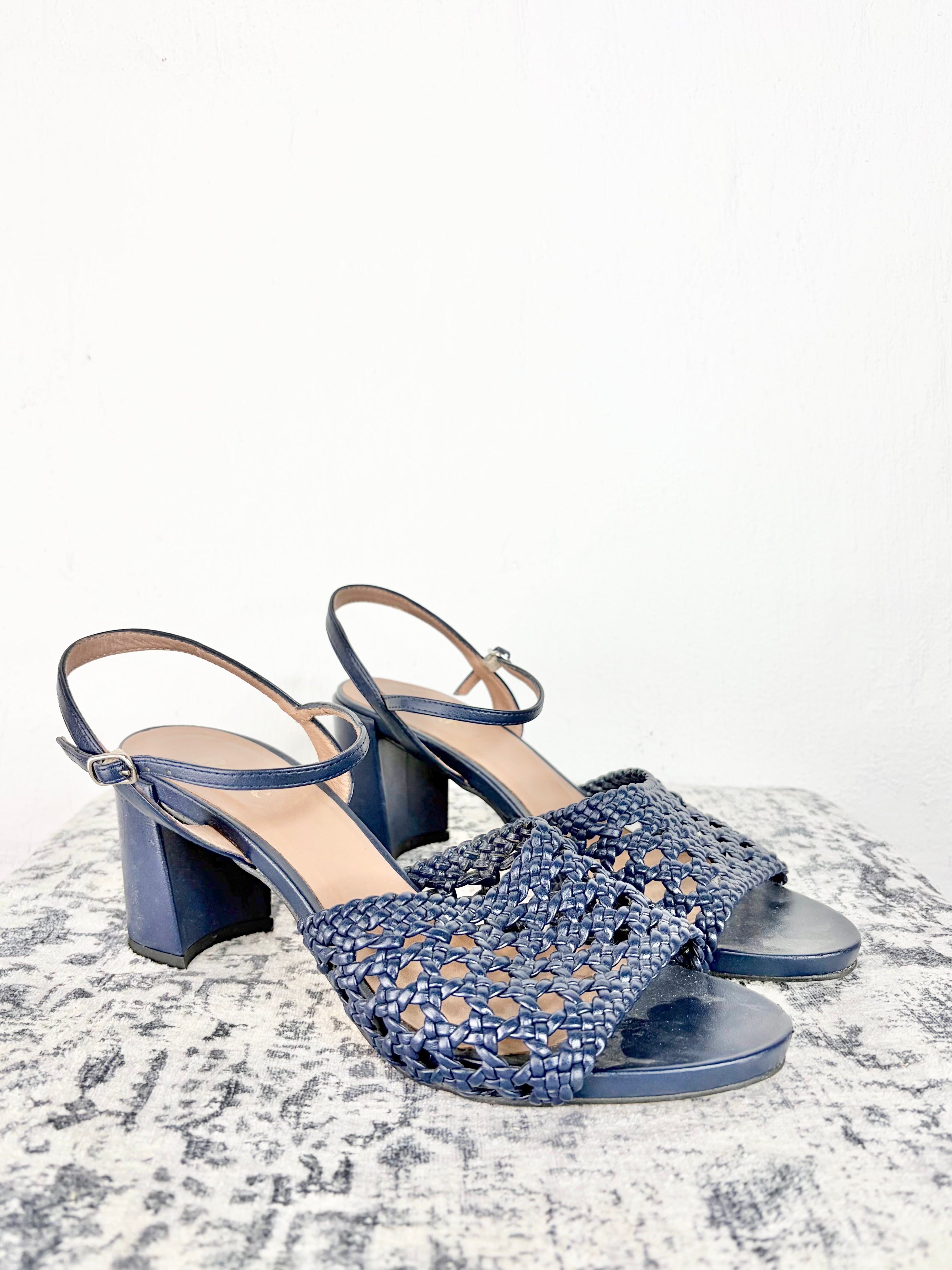 A pair of women's navy blue block-heel sandals with woven openwork straps and slingback ankle straps, displayed on a textured gray surface against a white background.