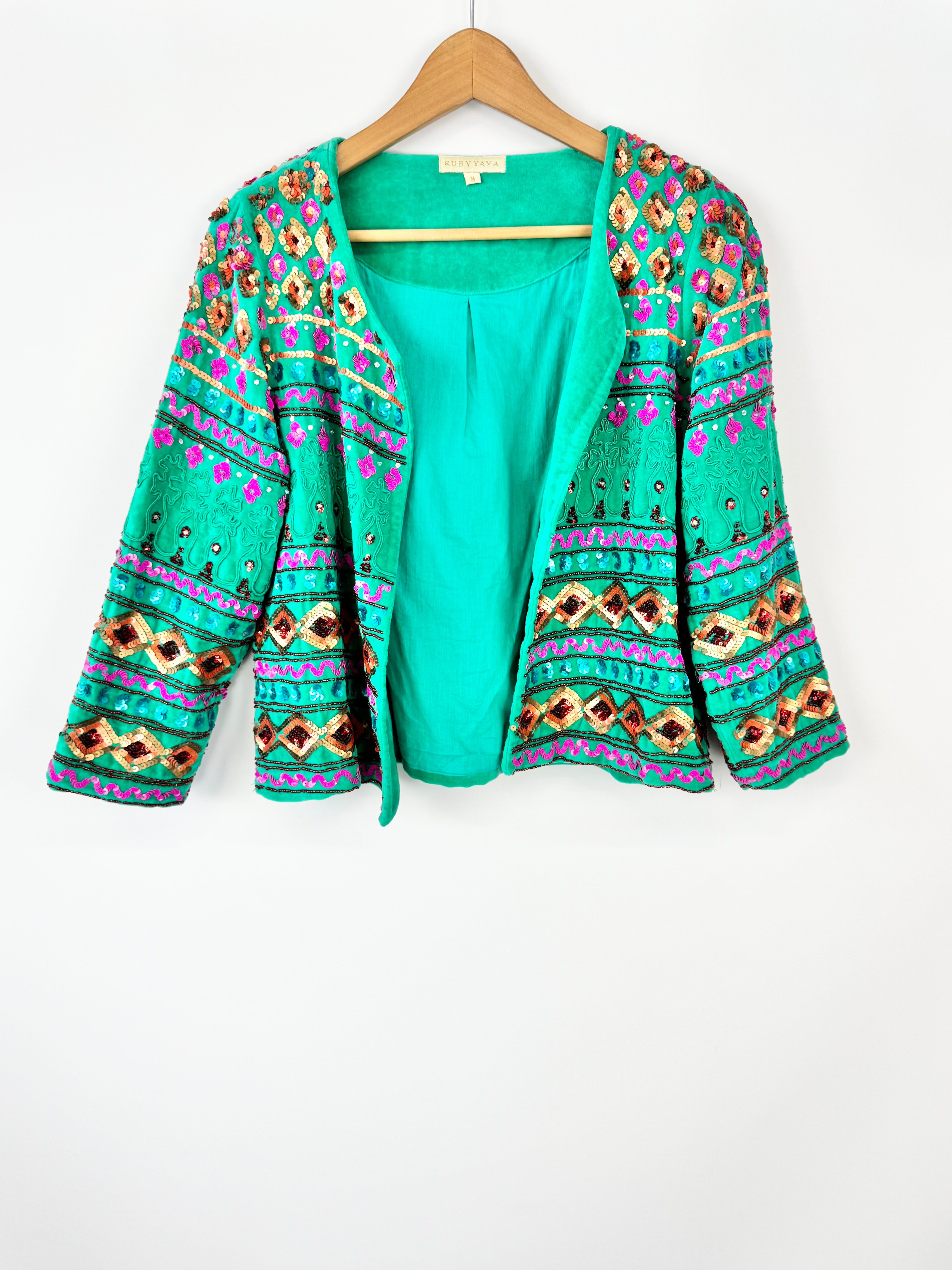 Green patterned cardigan on a hanger against a white background