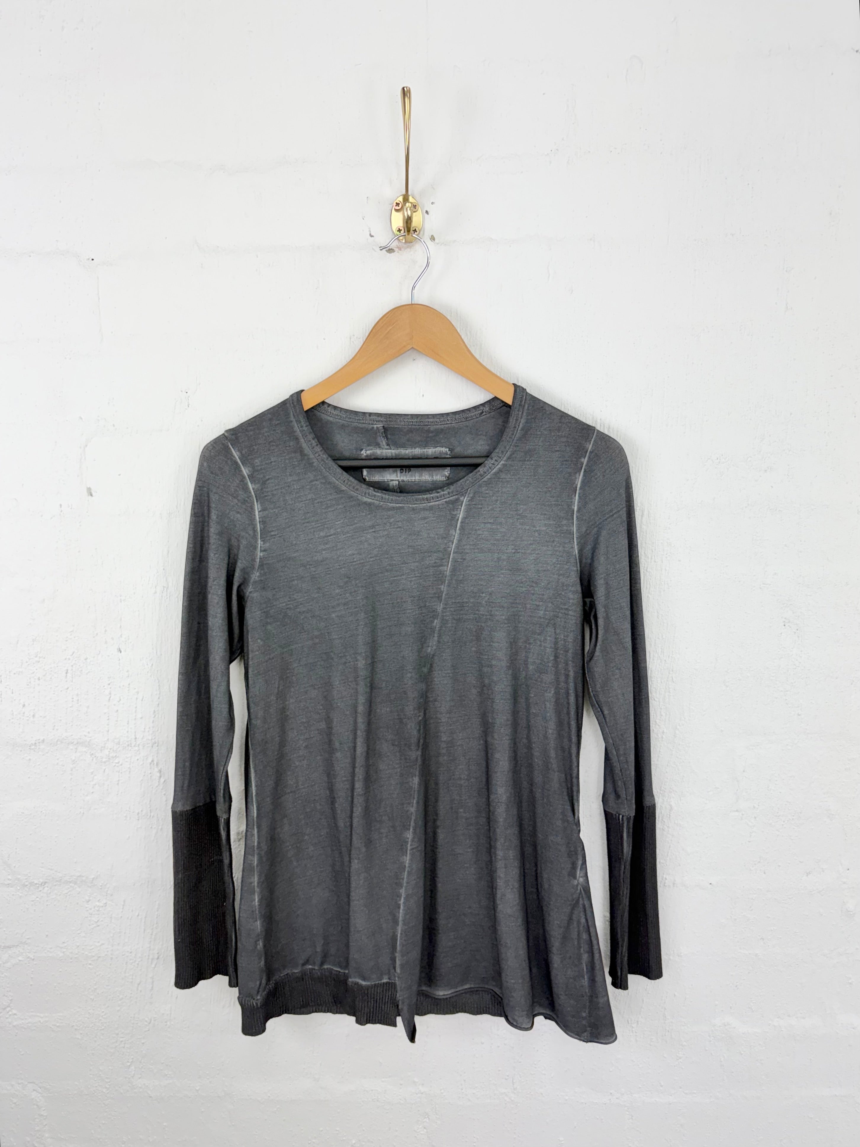 A dark gray long-sleeve top with a crew neck and diagonal seam detail, hanging on a wooden hanger against a white brick wall.