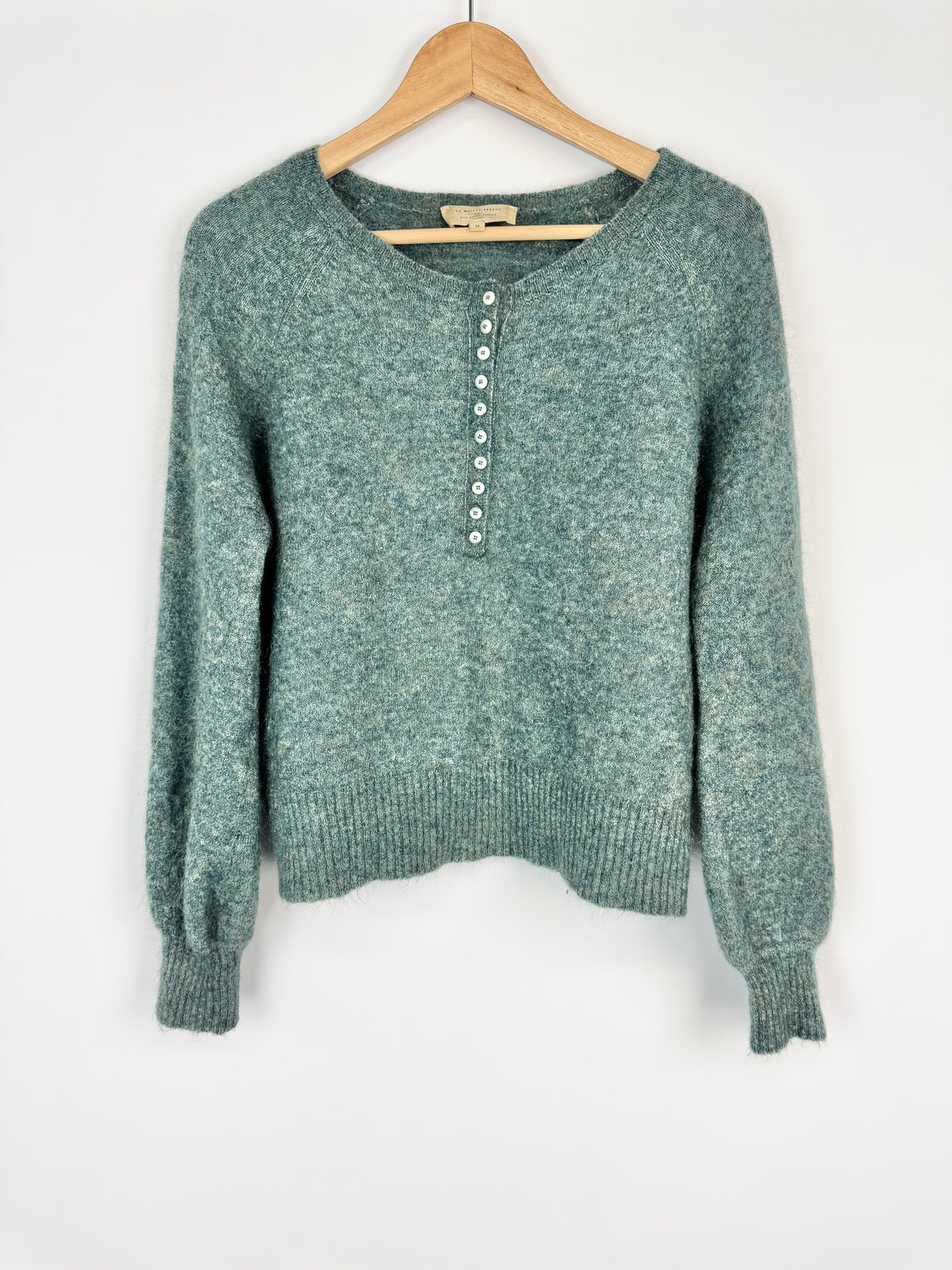 Green sweater on a wooden hanger against a white background