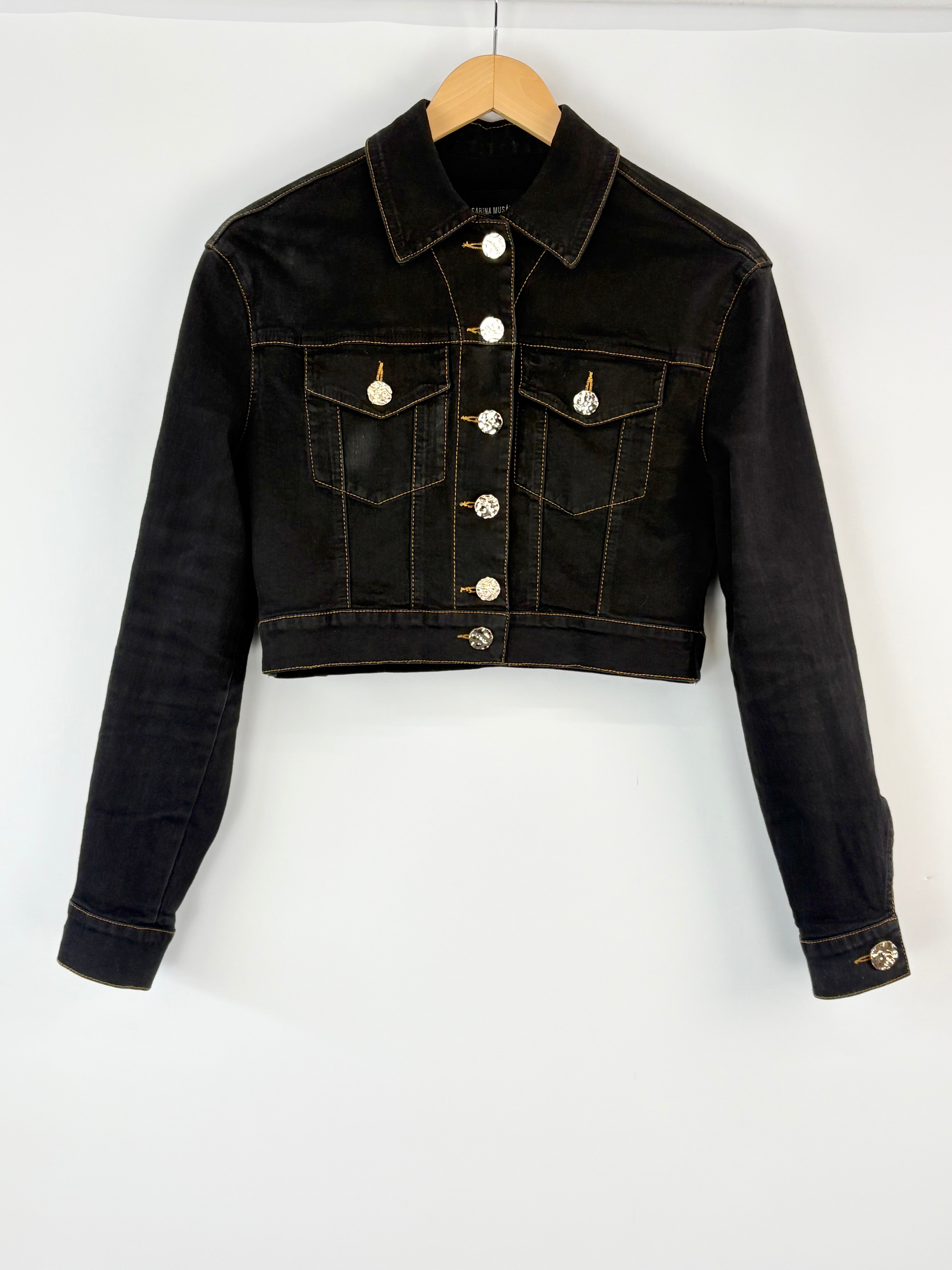 Black denim jacket on a wooden hanger against a white background