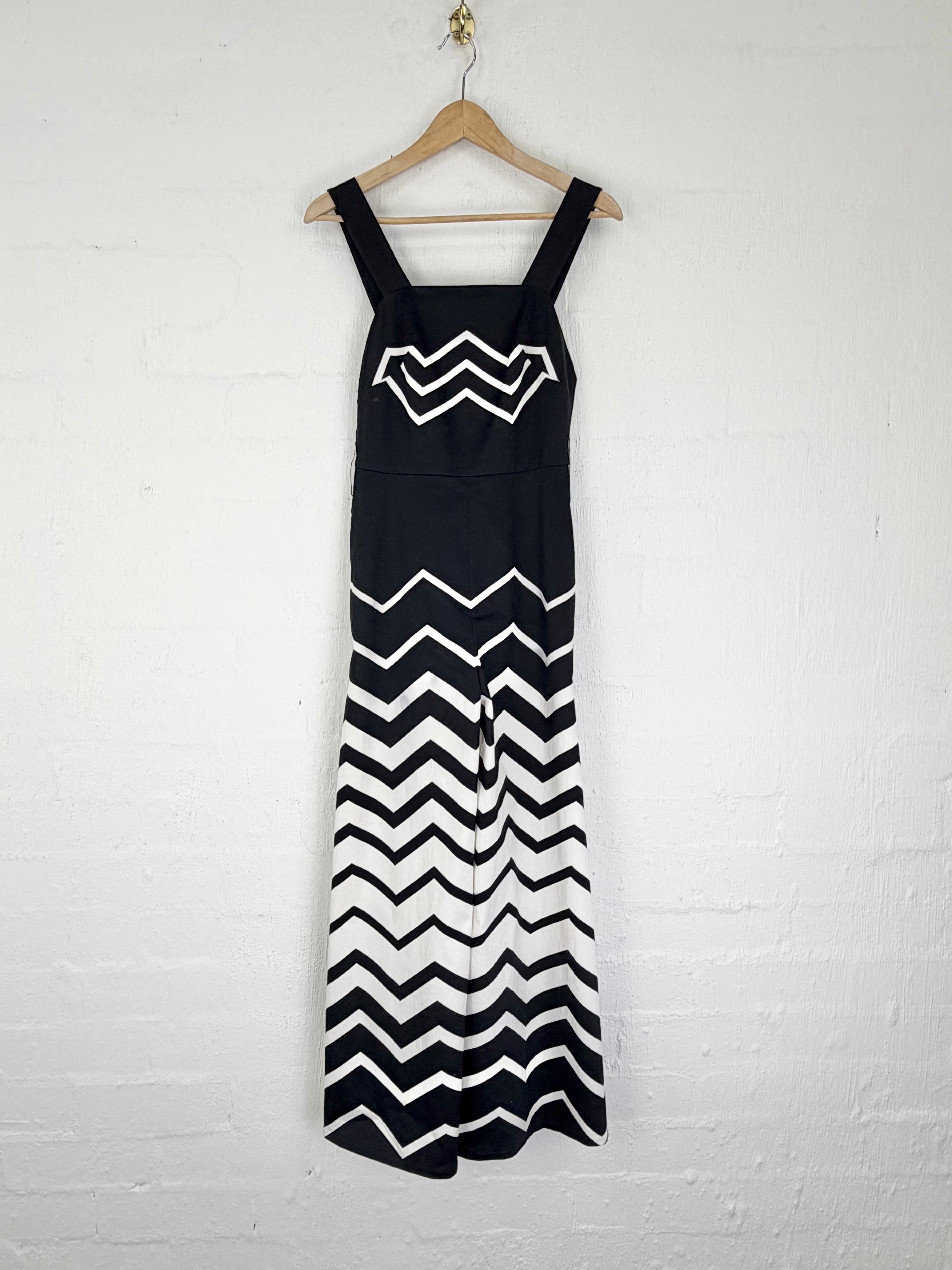 A sleeveless black dress with white chevron patterns hanging on a wooden hanger against a white brick wall.