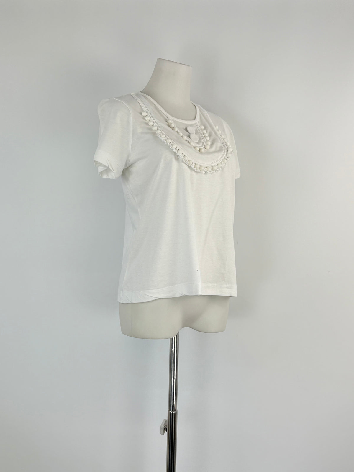 White blouse with lace details on a mannequin against a plain background