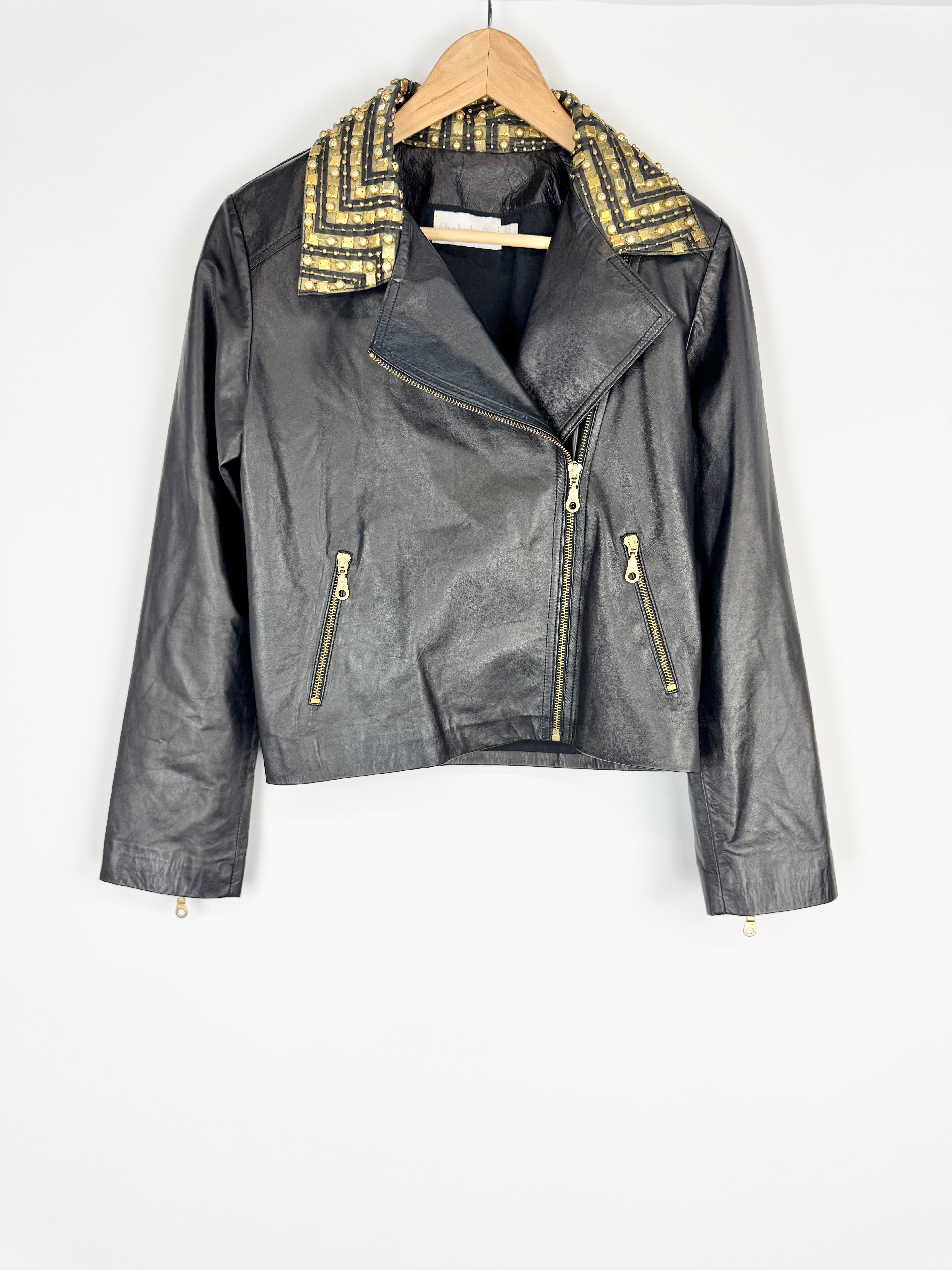 Black leather jacket with gold accents on a hanger against a white background