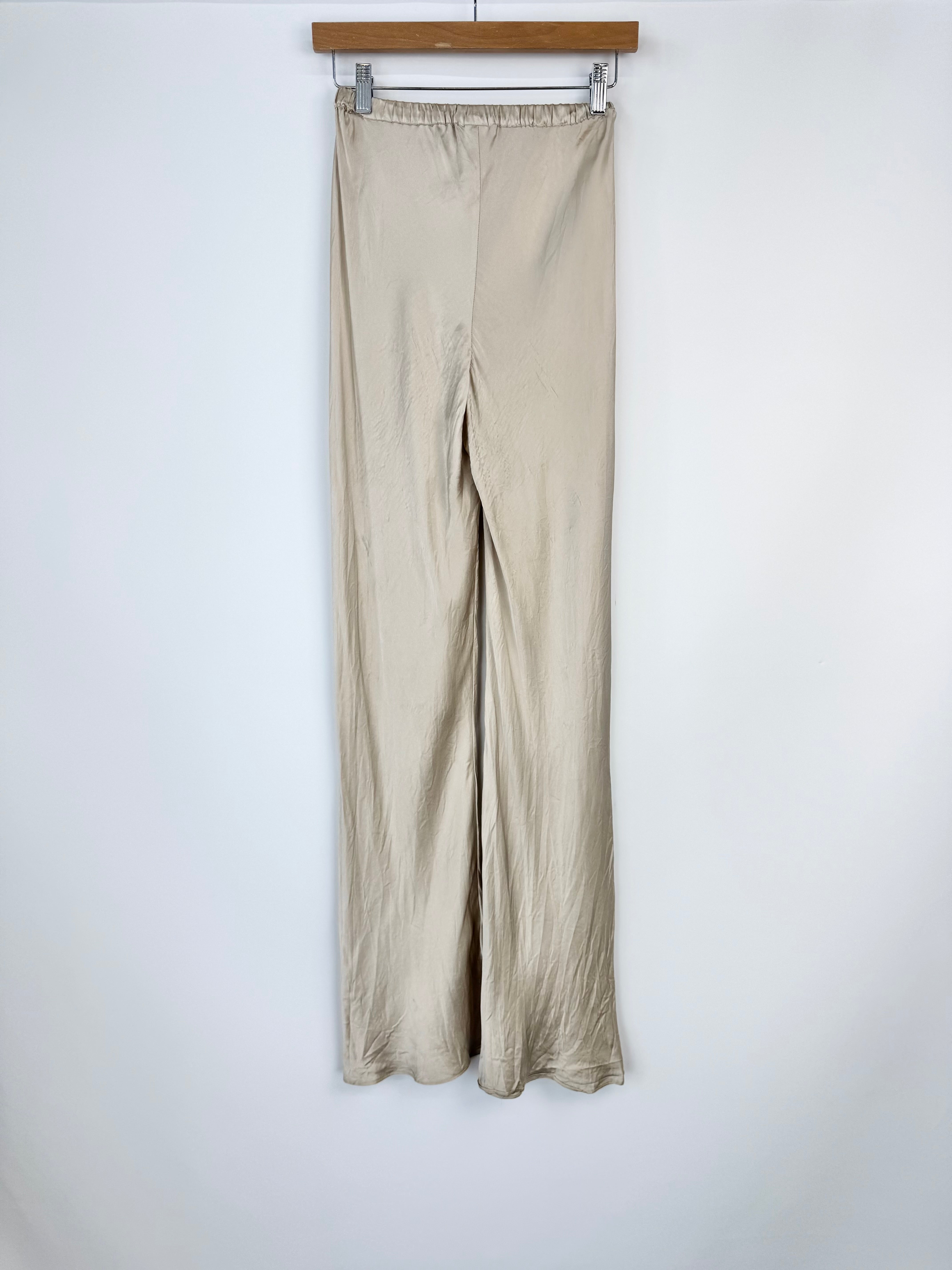 Beige pants hanging on a wooden hanger against a white wall