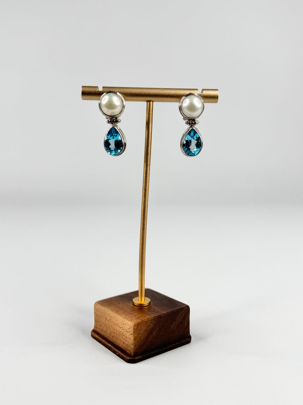Pair of earrings on a gold and wooden stand against a white background