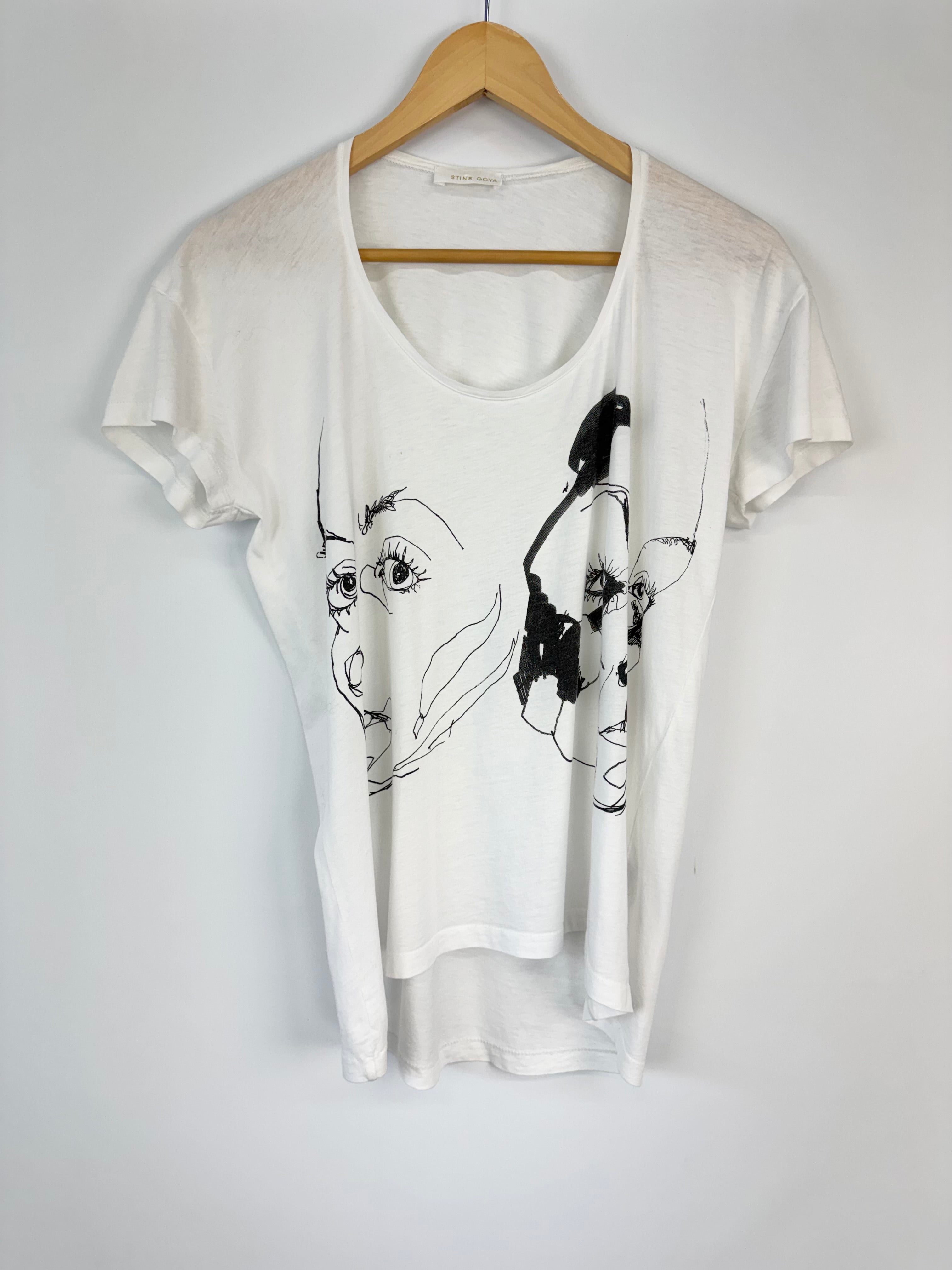White t-shirt with black graphics on a wooden hanger against a white background