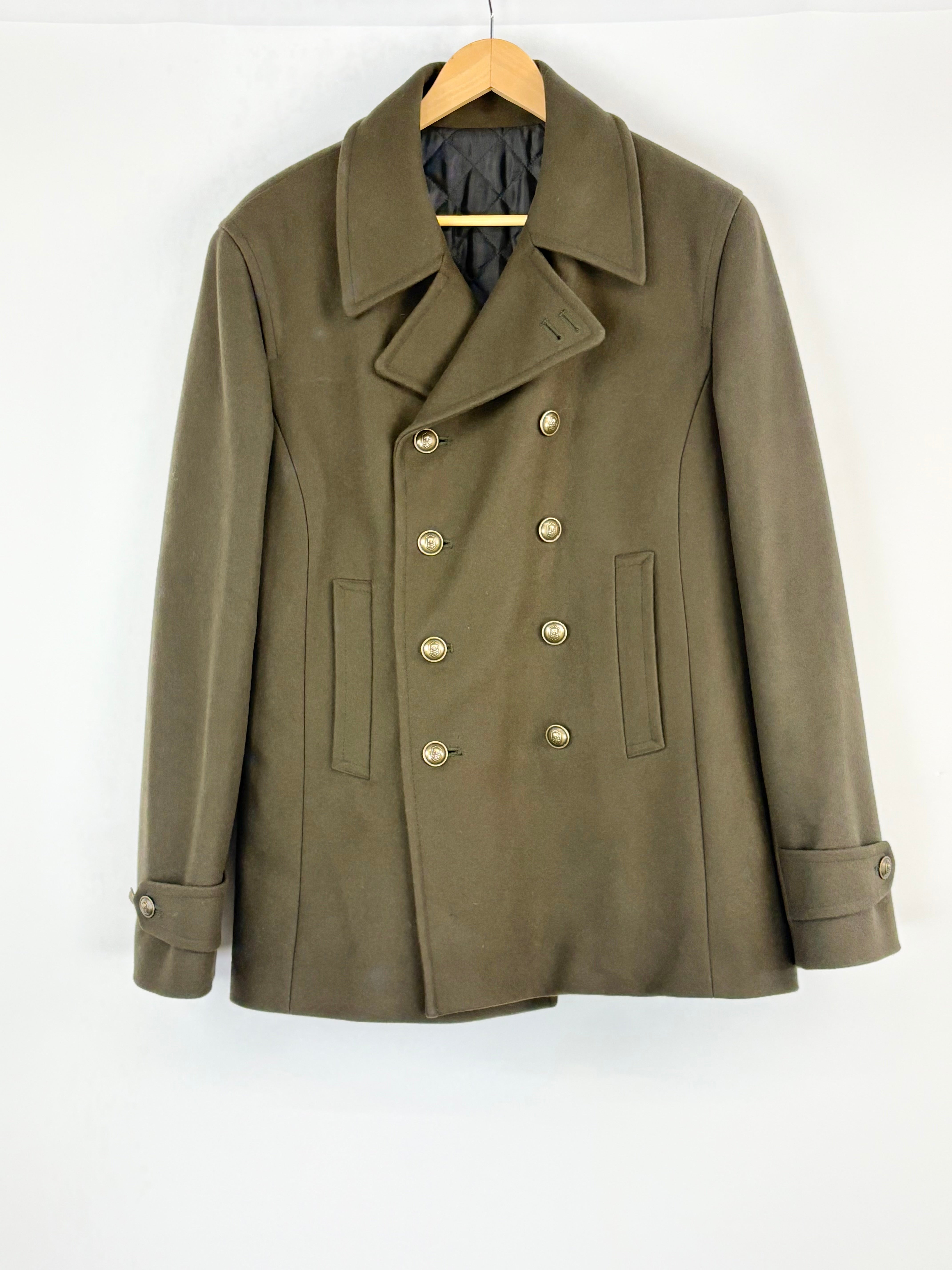 Green peacoat on a wooden hanger against a white background