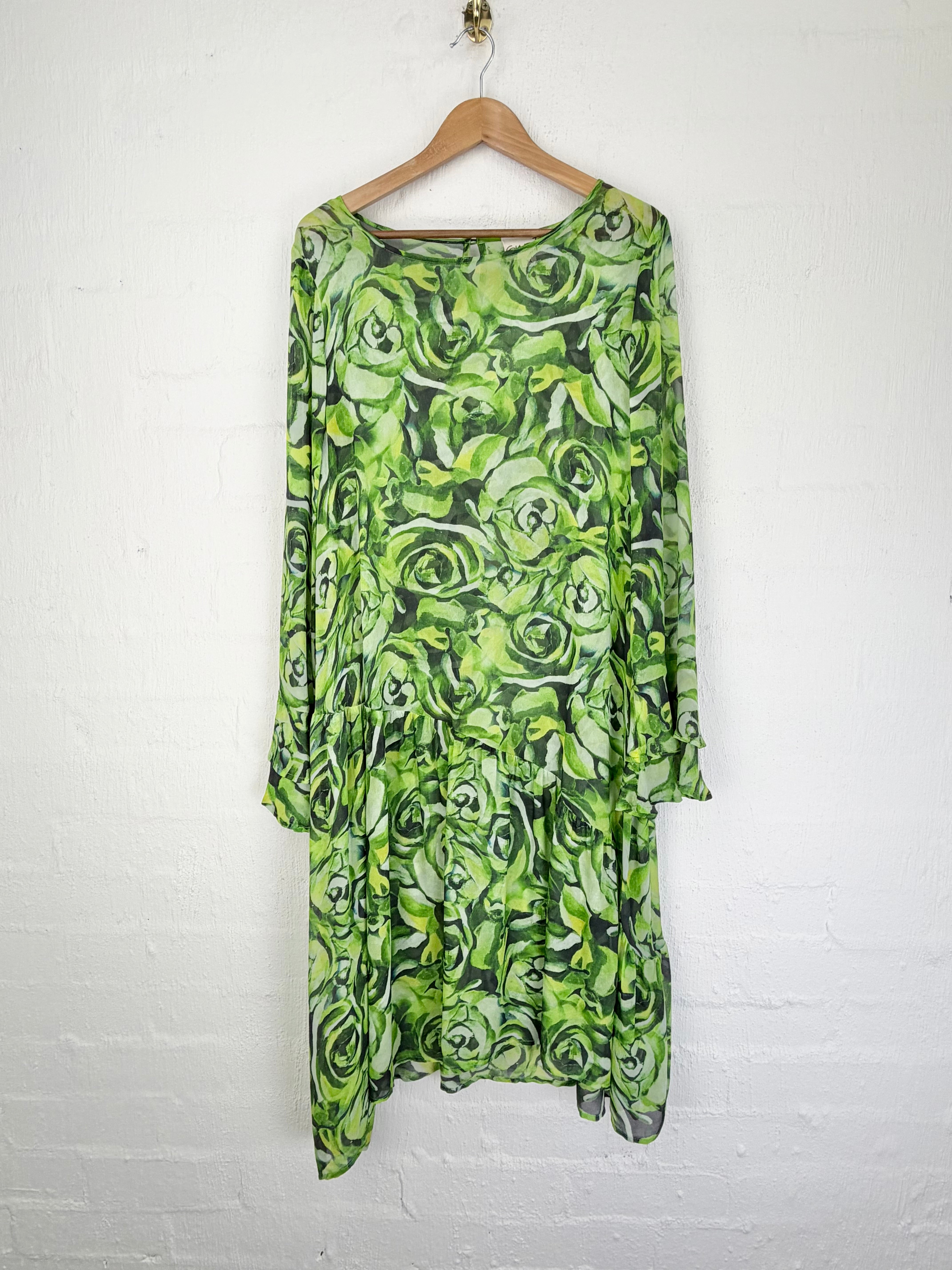 A green and black floral print long-sleeve dress hanging on a wooden hanger against a white brick wall.