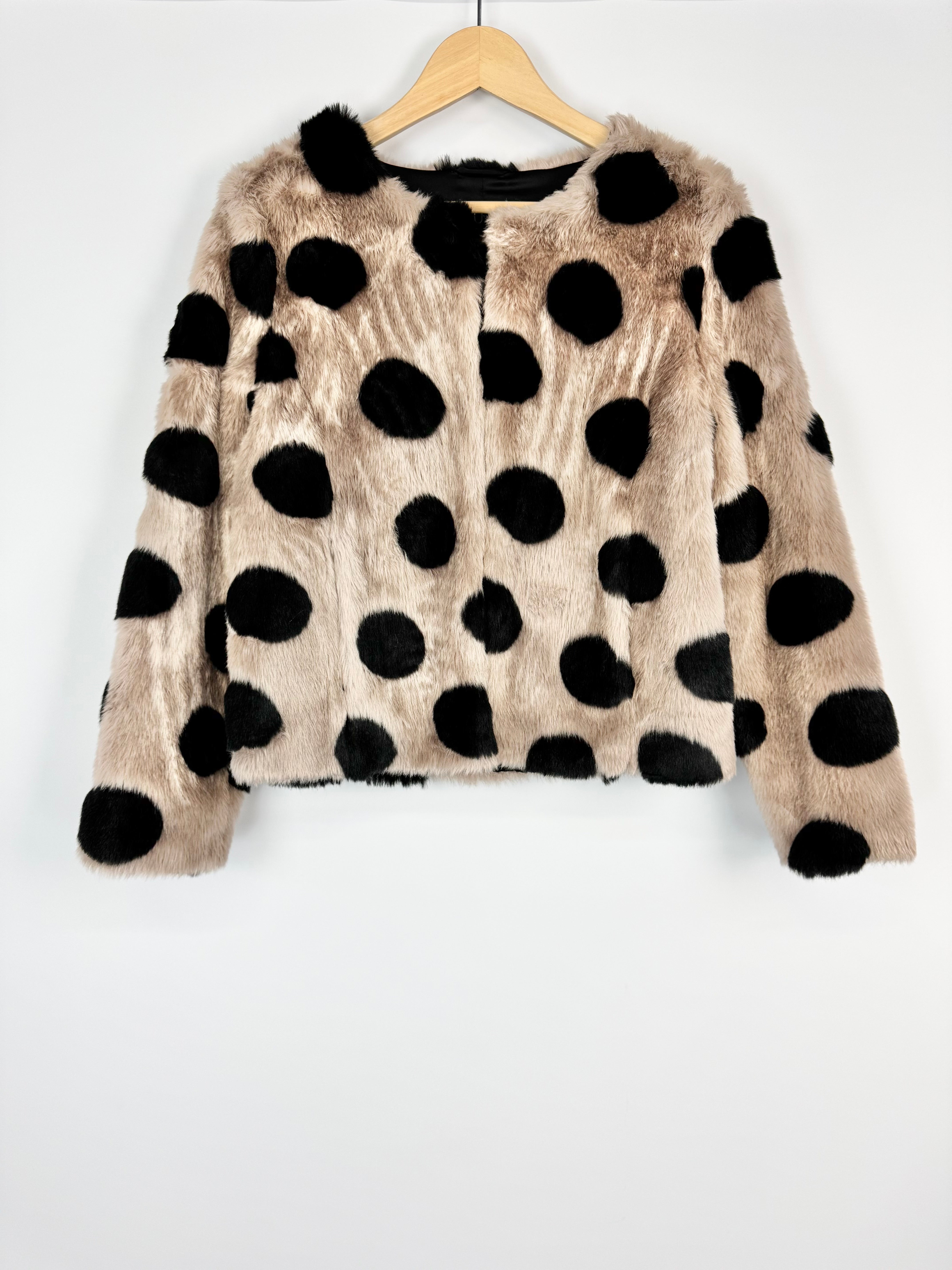Beige sweater with black polka dots on a wooden hanger against a white background