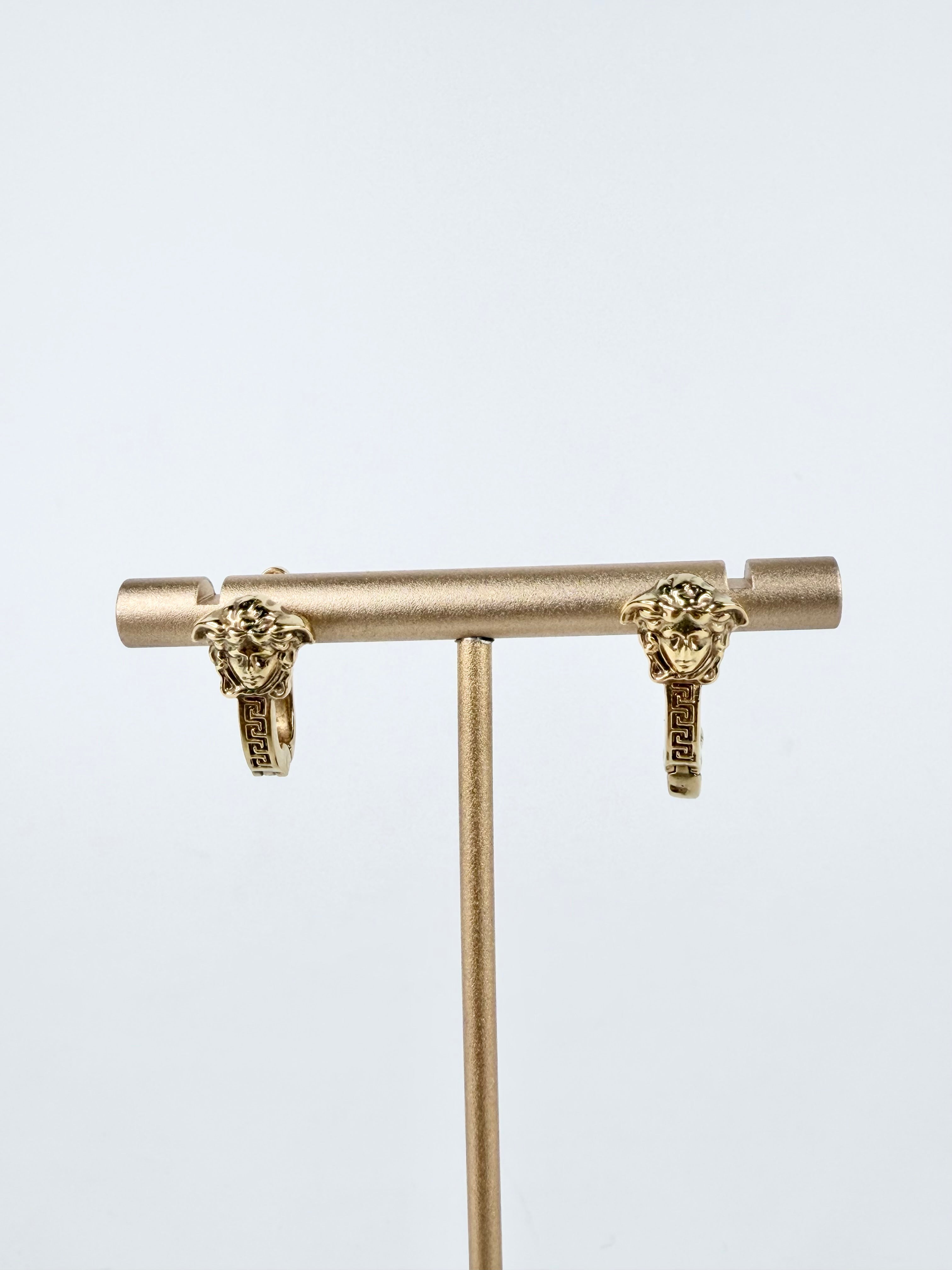 Gold T-bar earring with lion head designs on a light gray background