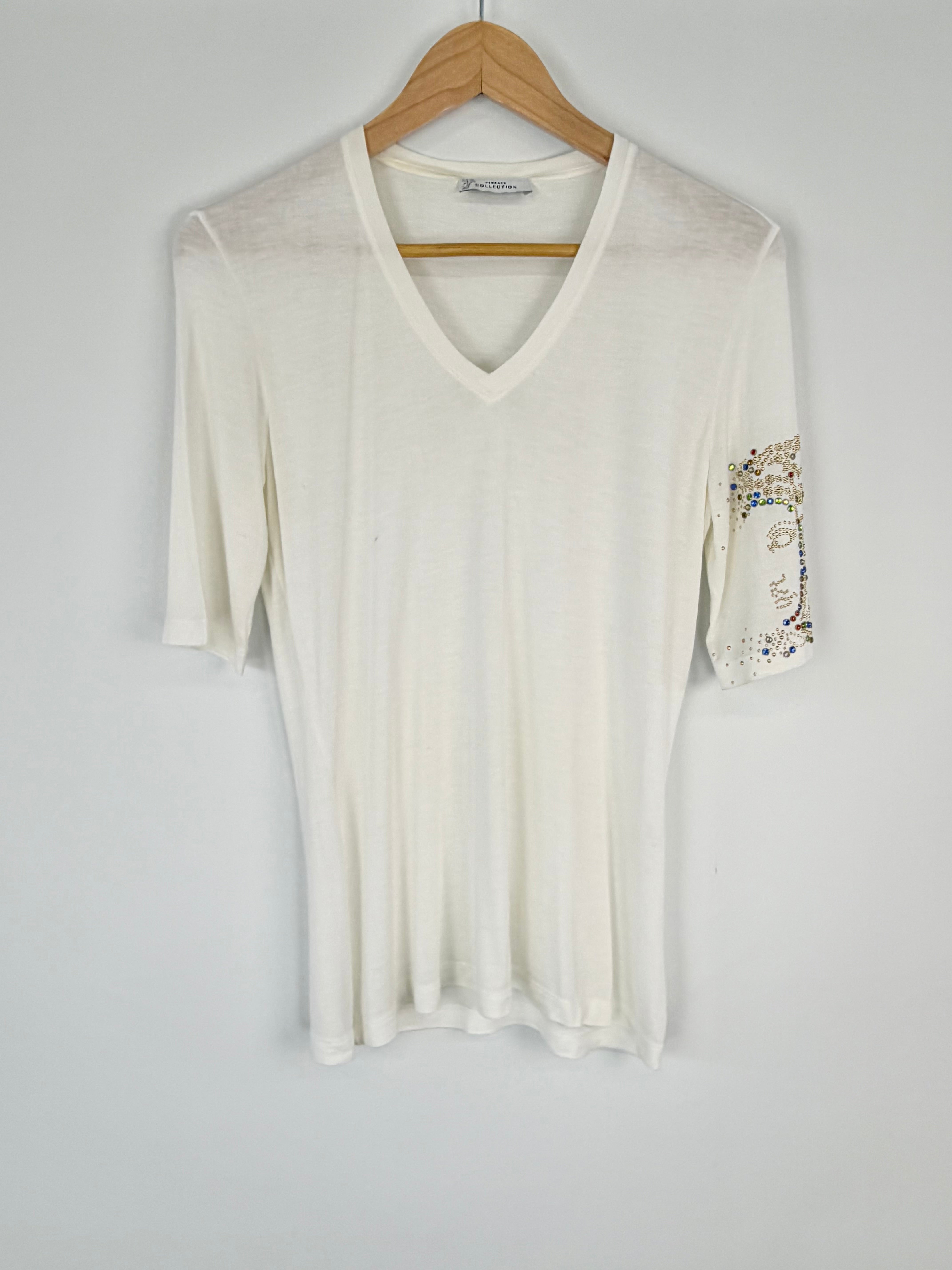 White long-sleeve top with embellishments on a hanger against a gray background