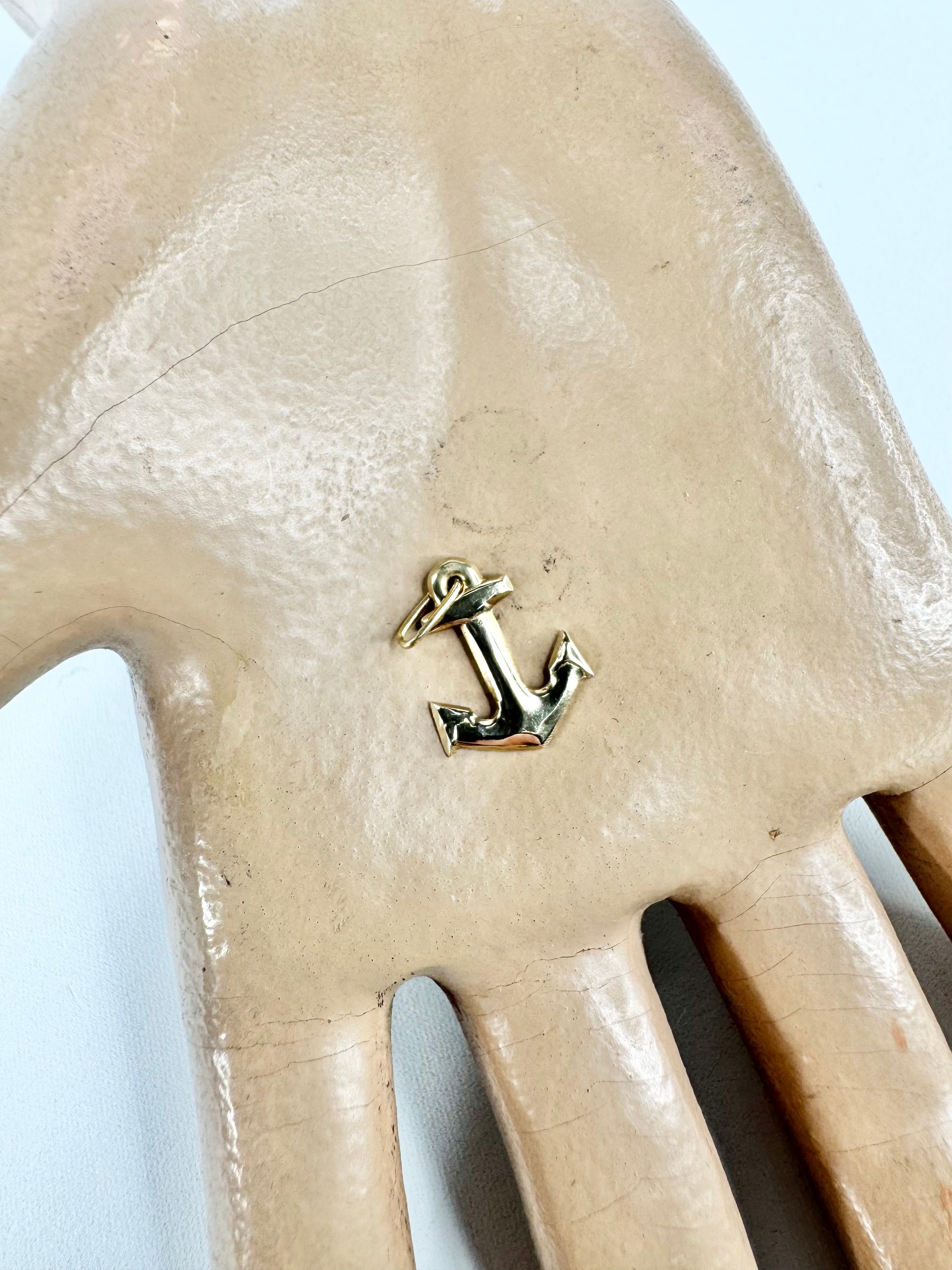 Gold anchor charm on a beige leather glove against a light blue background