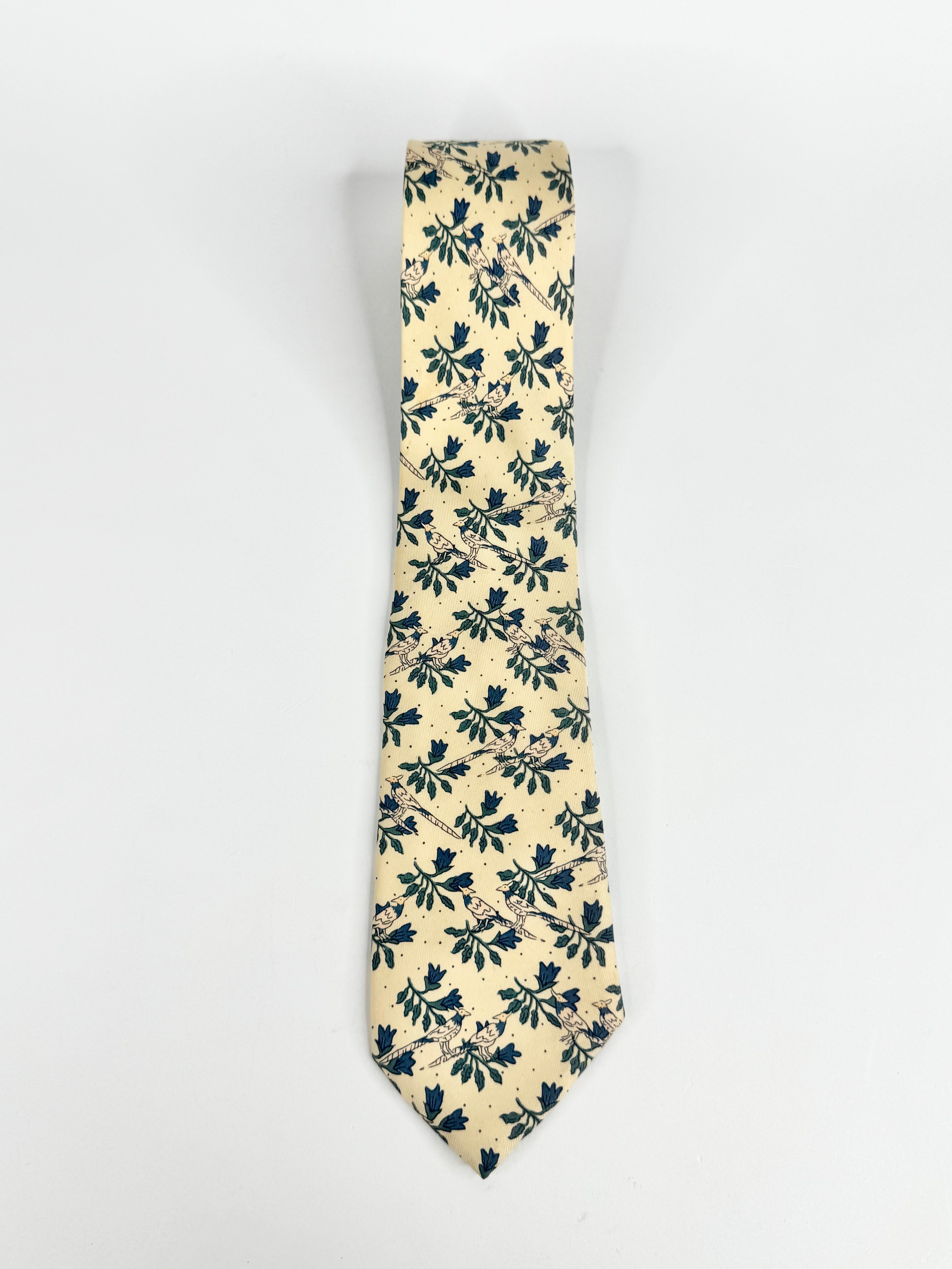 A cream colour tie with bird patterns on a white background