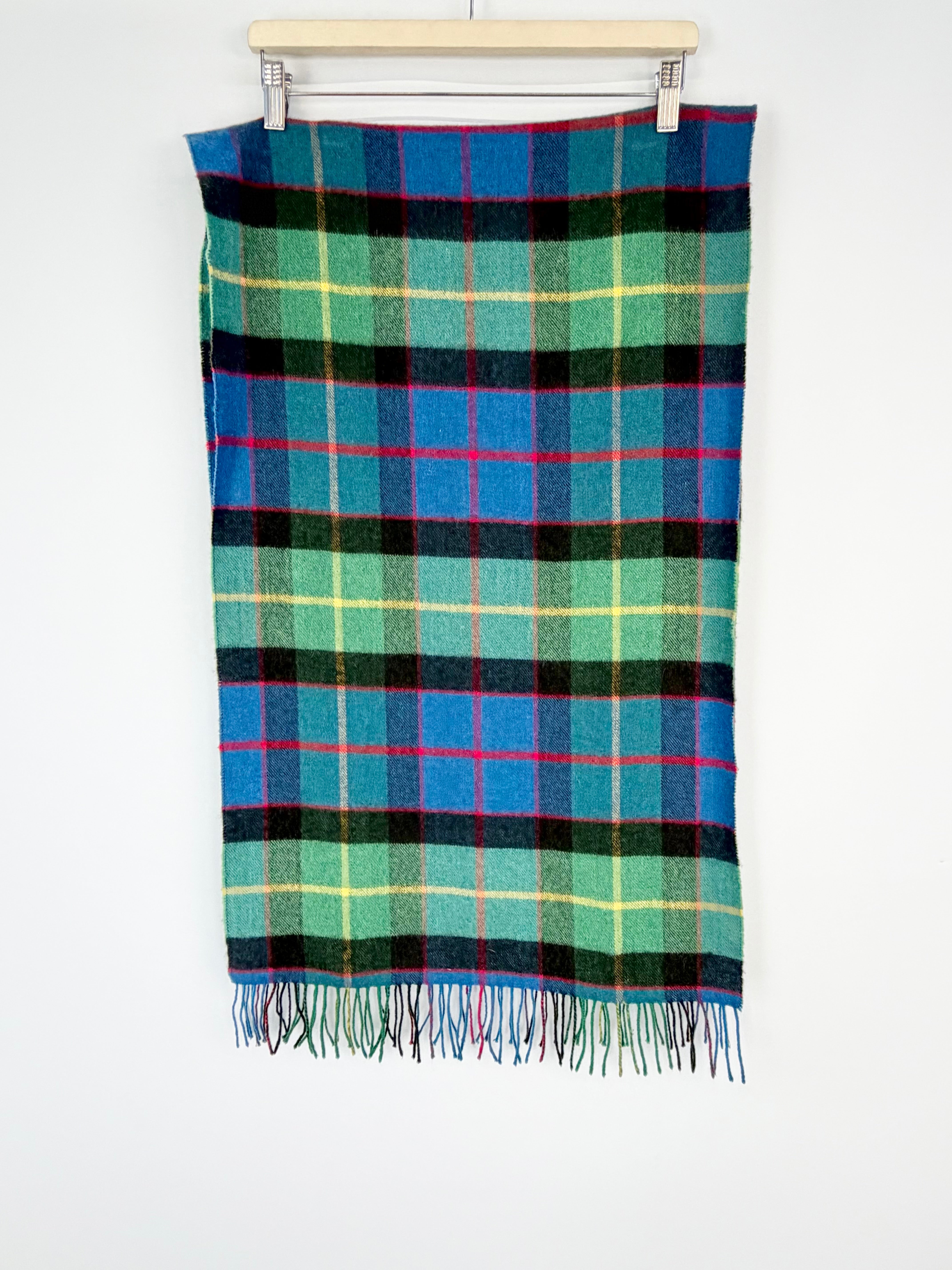 Plaid blanket with blue, green, and black colors on a wooden hanger against a white background