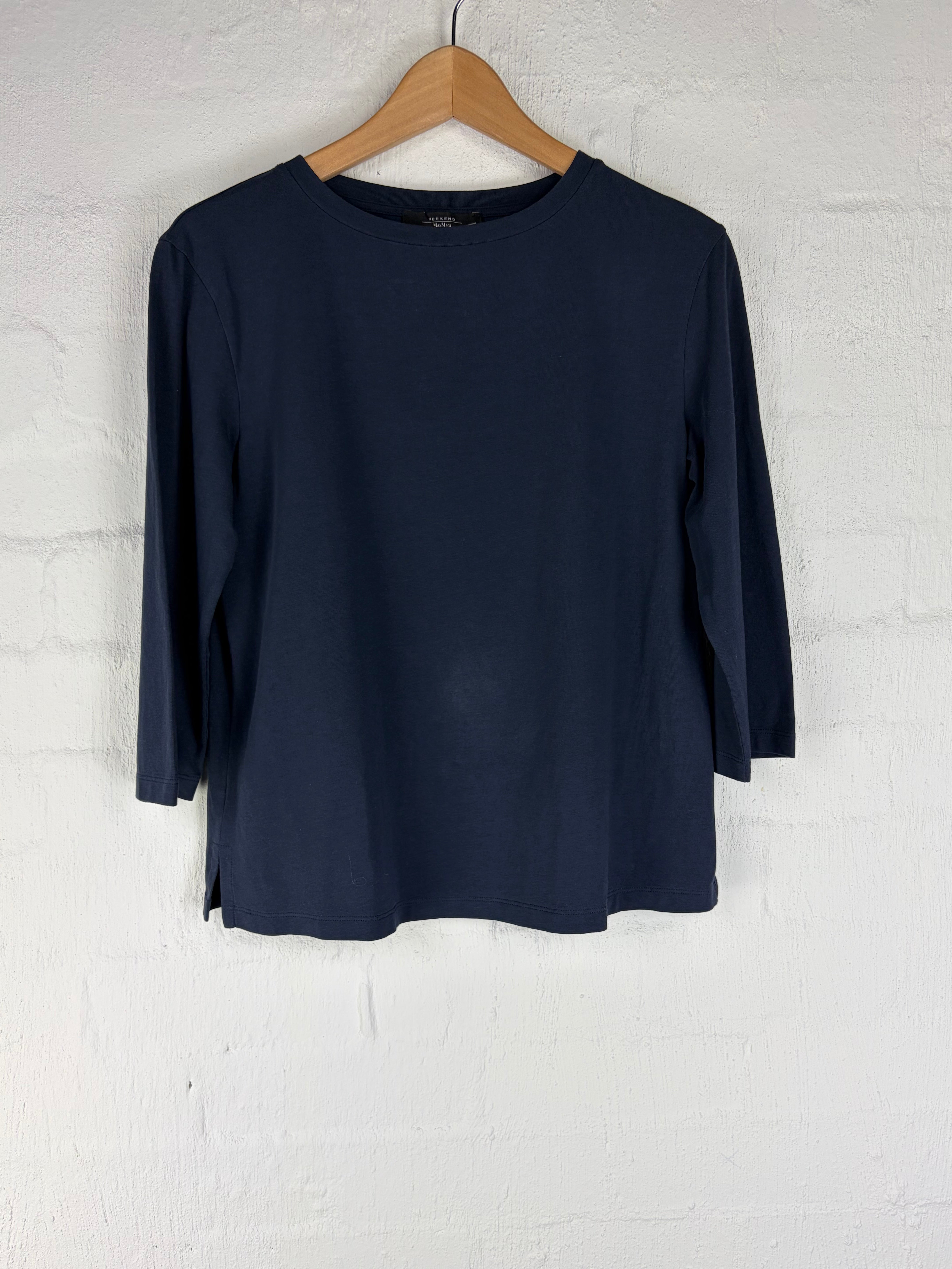 A navy blue long-sleeve top laid flat on a light wood hanger against a white textured wall.