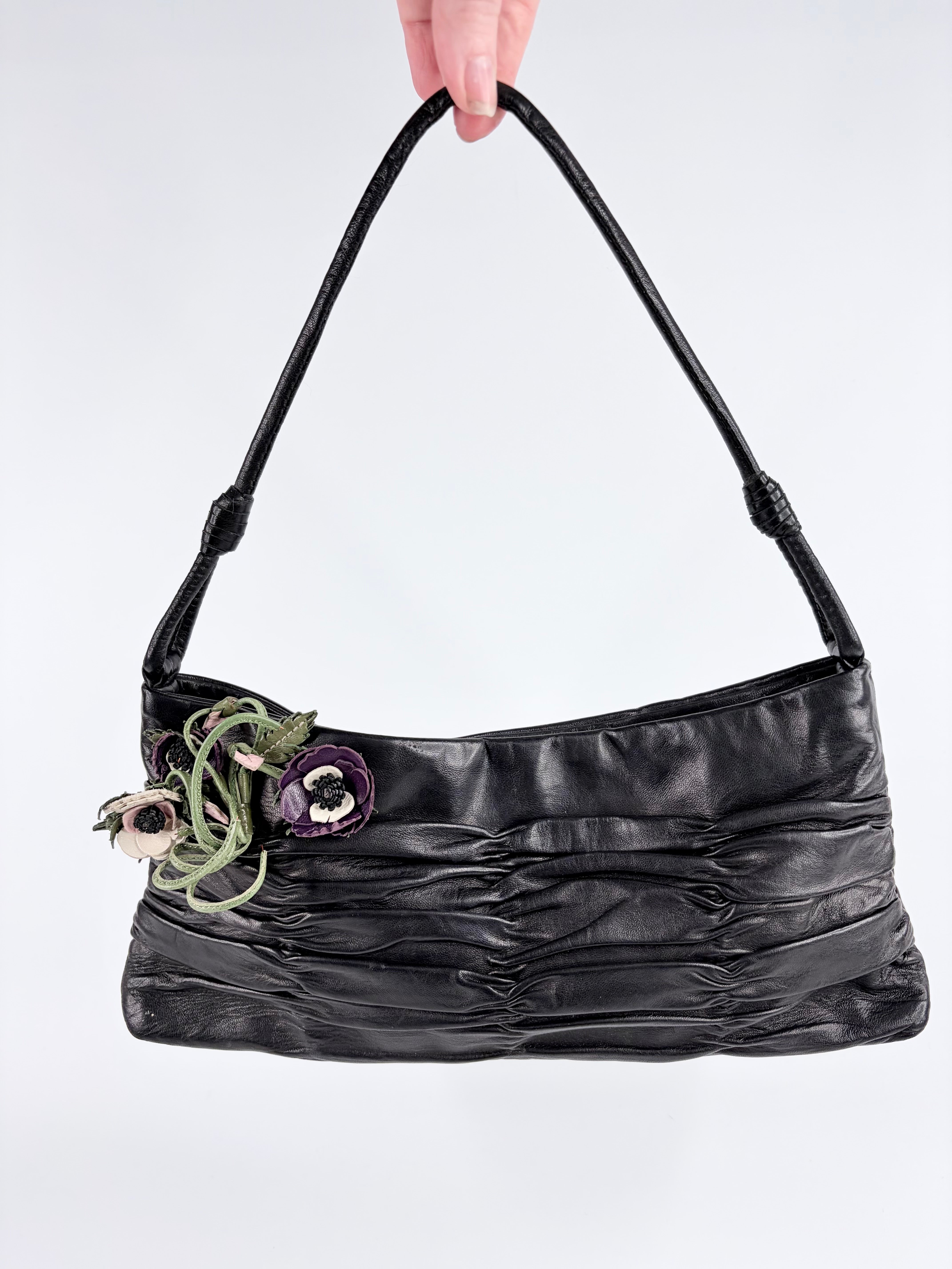 Black handbag with floral details held by a hand against a white background