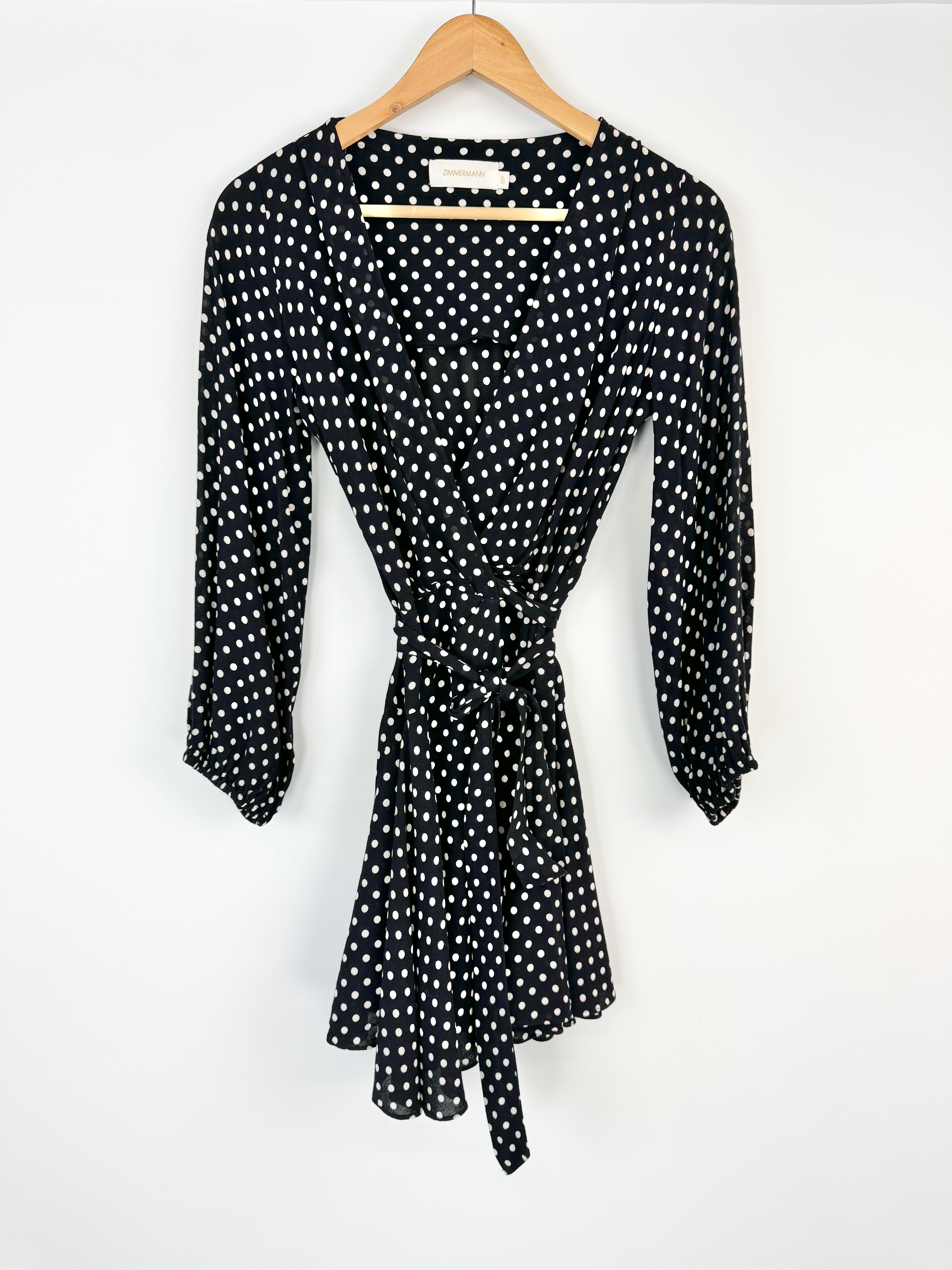 Black dress with white polka dots on a hanger against a white background