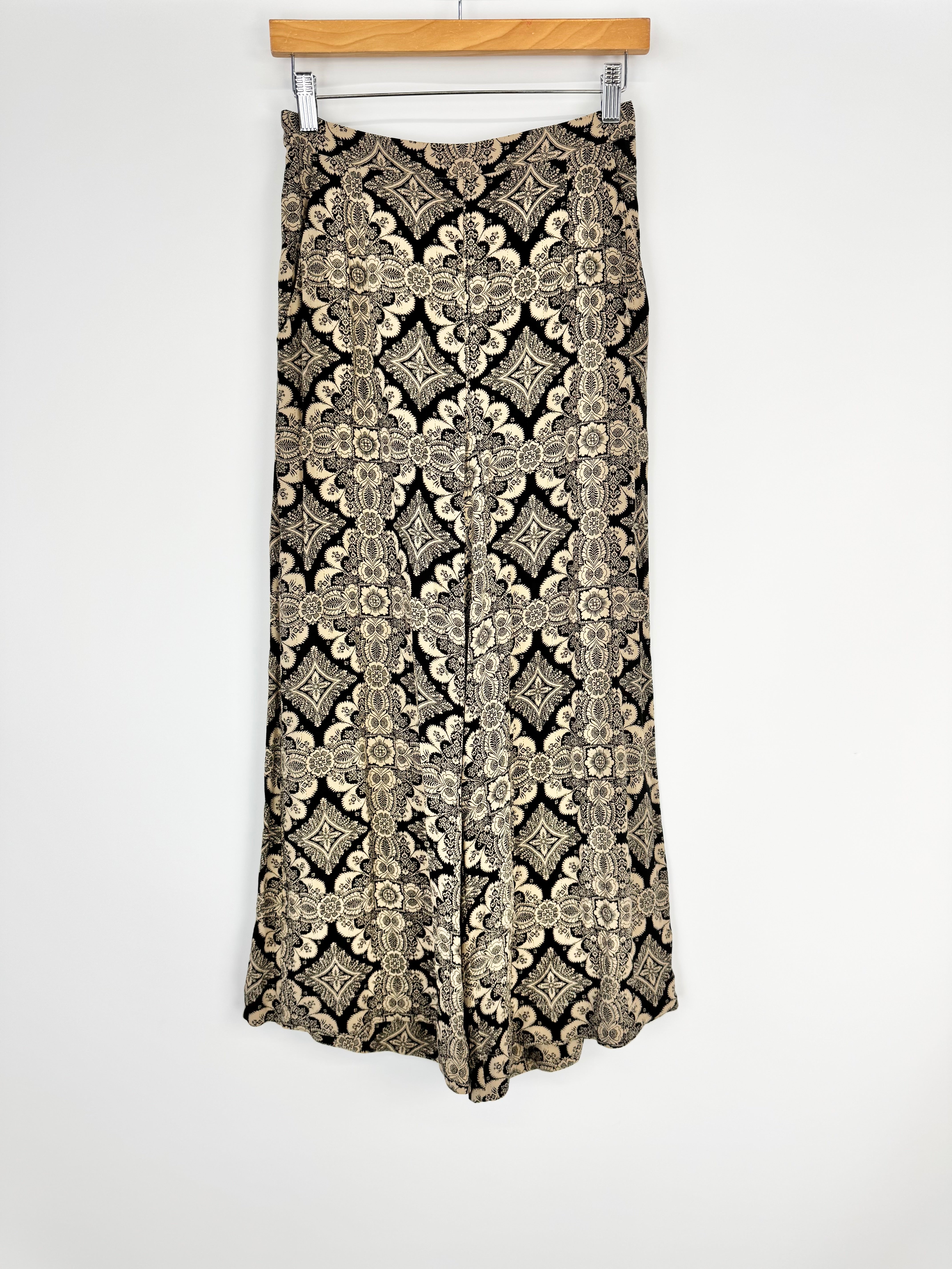 Patterned wide leg slacks hanging on a wooden hanger against a white background