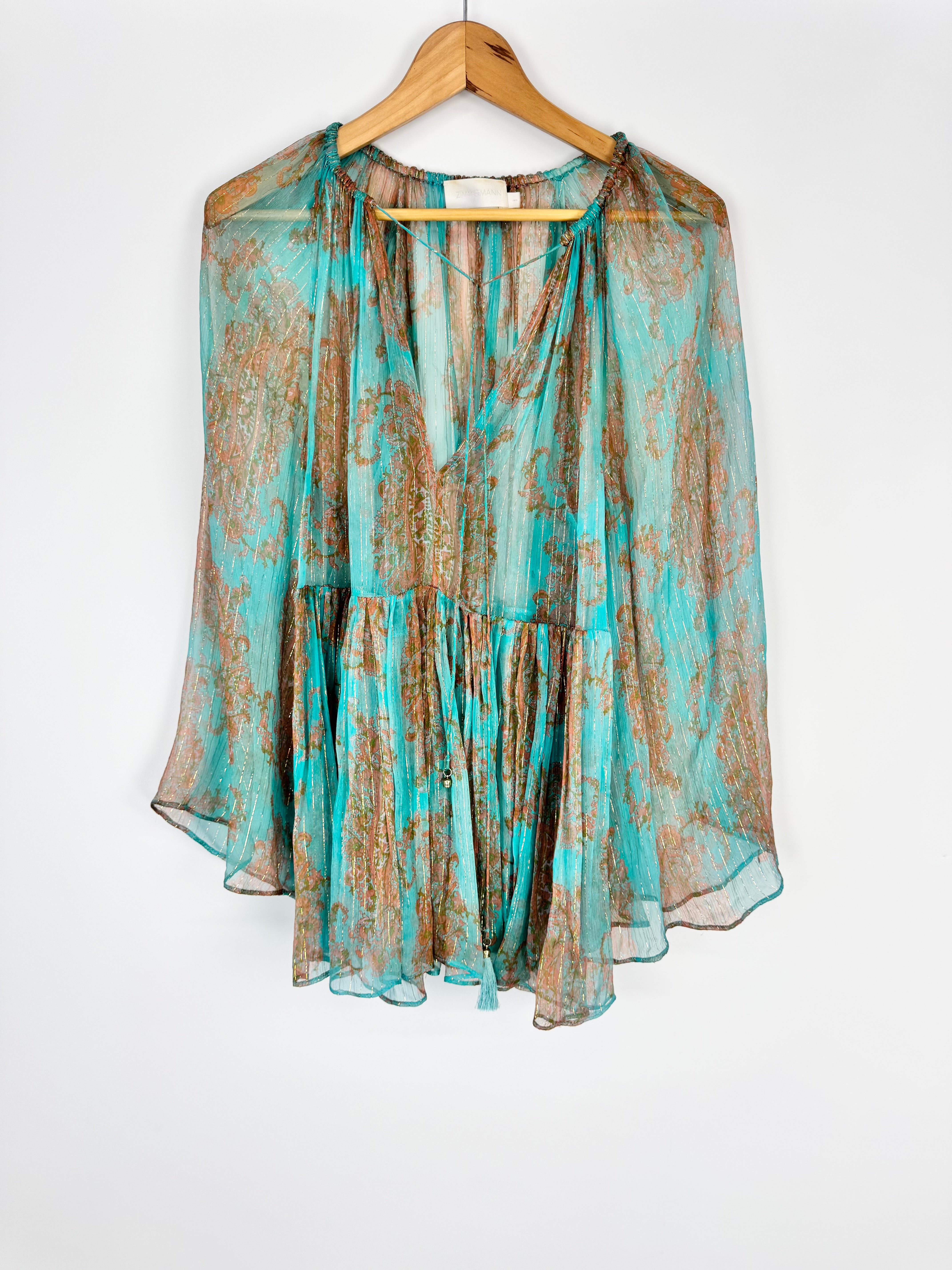 Light blue and brown patterned blouse on a hanger against a white background