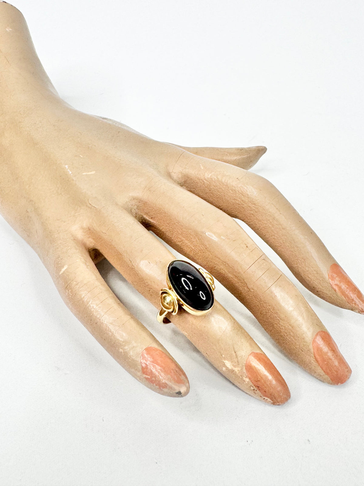 Mannequin hand wearing a deep almost black red crystal and gold ring on a white background