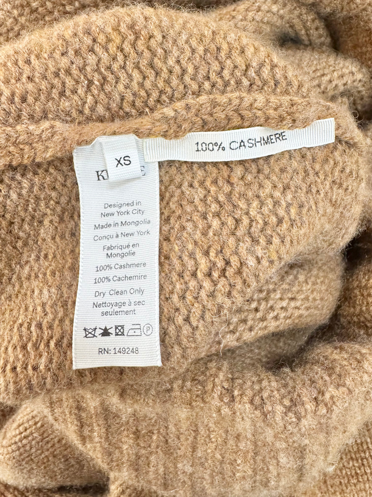 Close-up of a beige cashmere fabric with a label indicating '100% Cashmere' and size 'XS'.