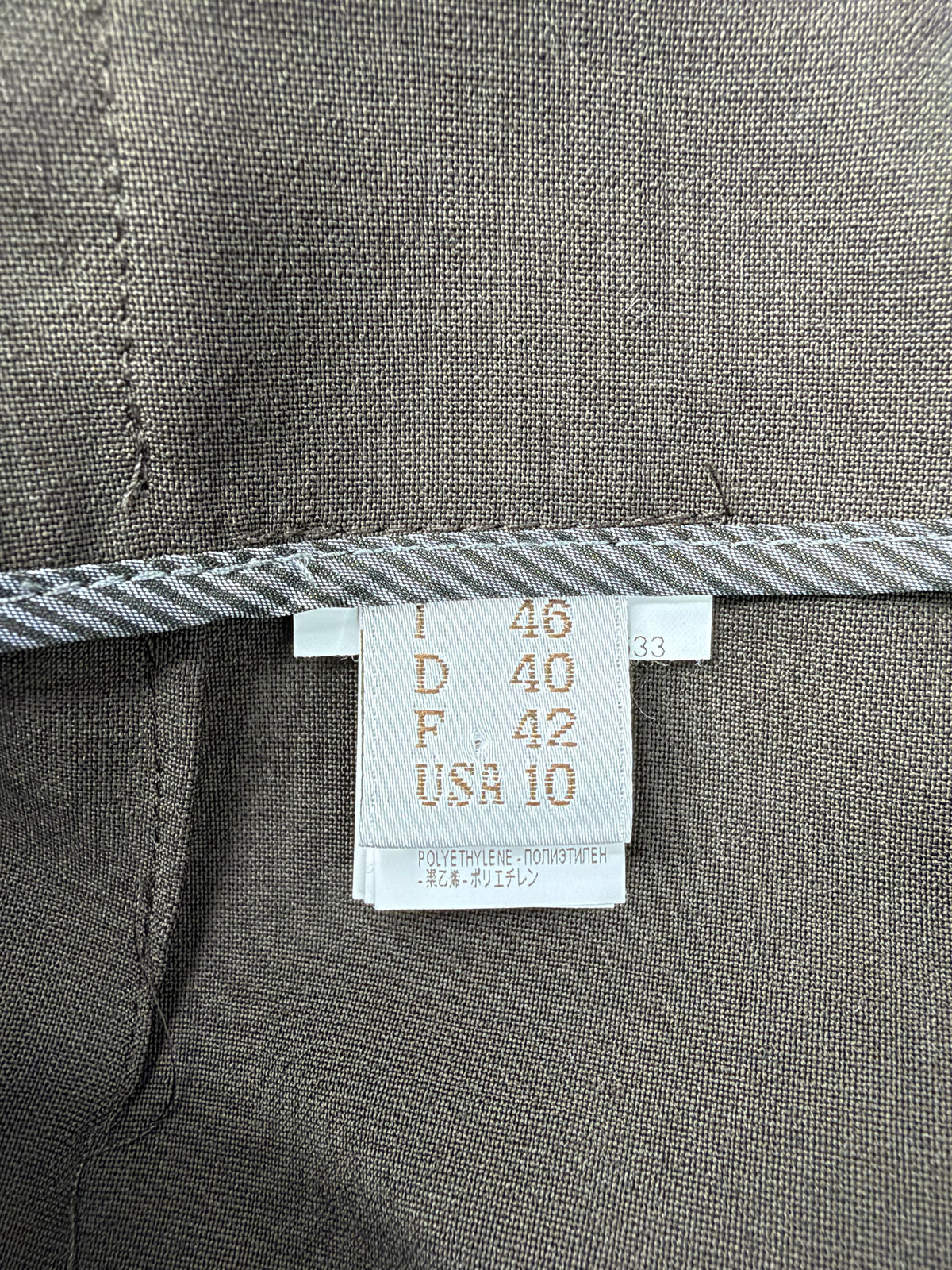 Close-up of a garment's interior size label sewn onto a gray textured fabric, showing measurements for size 46, 40, 42, and USA 10.