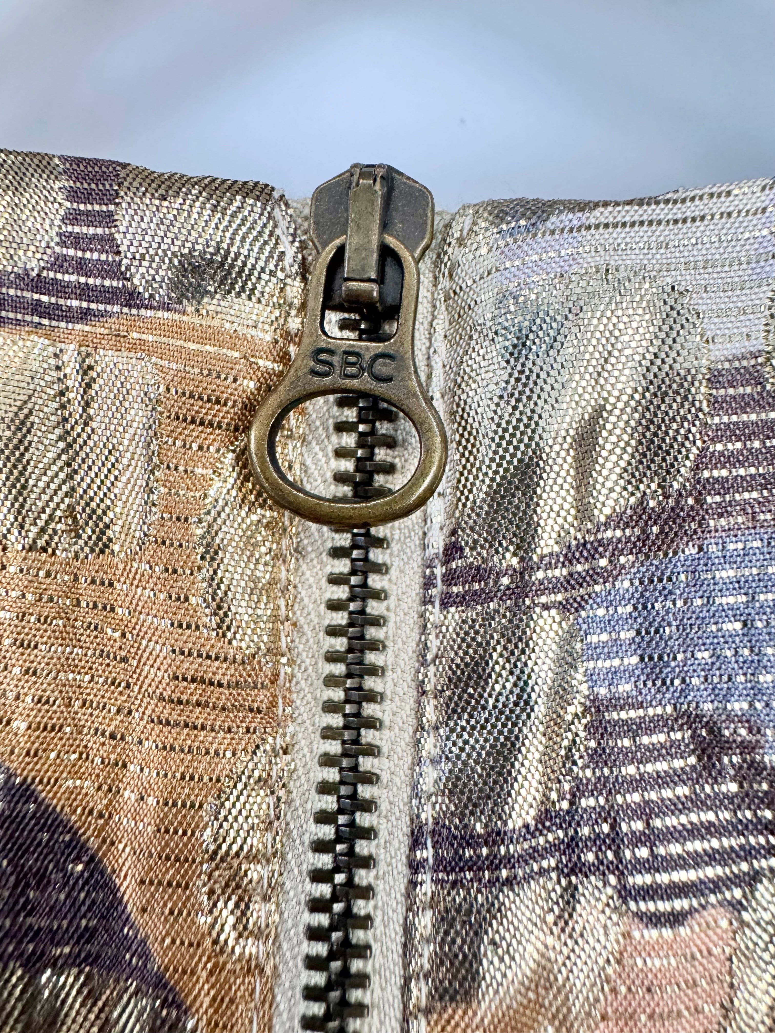 Close-up of a zipper on a plaid fabric background with 'SBC' branding.