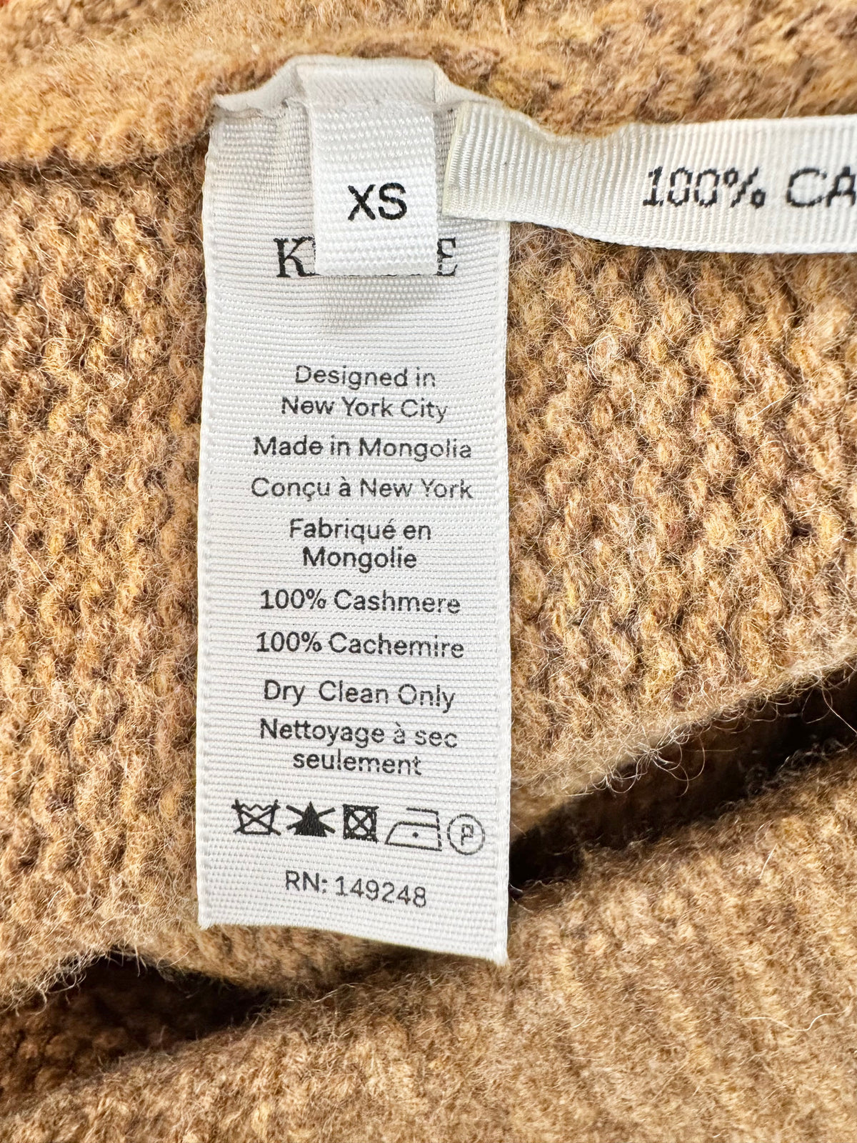Close-up of a cashmere garment label with text and symbols on a textured fabric background.
