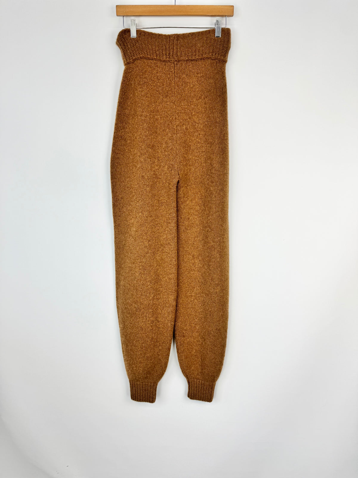 Brown knitted pants on a hanger against a white background