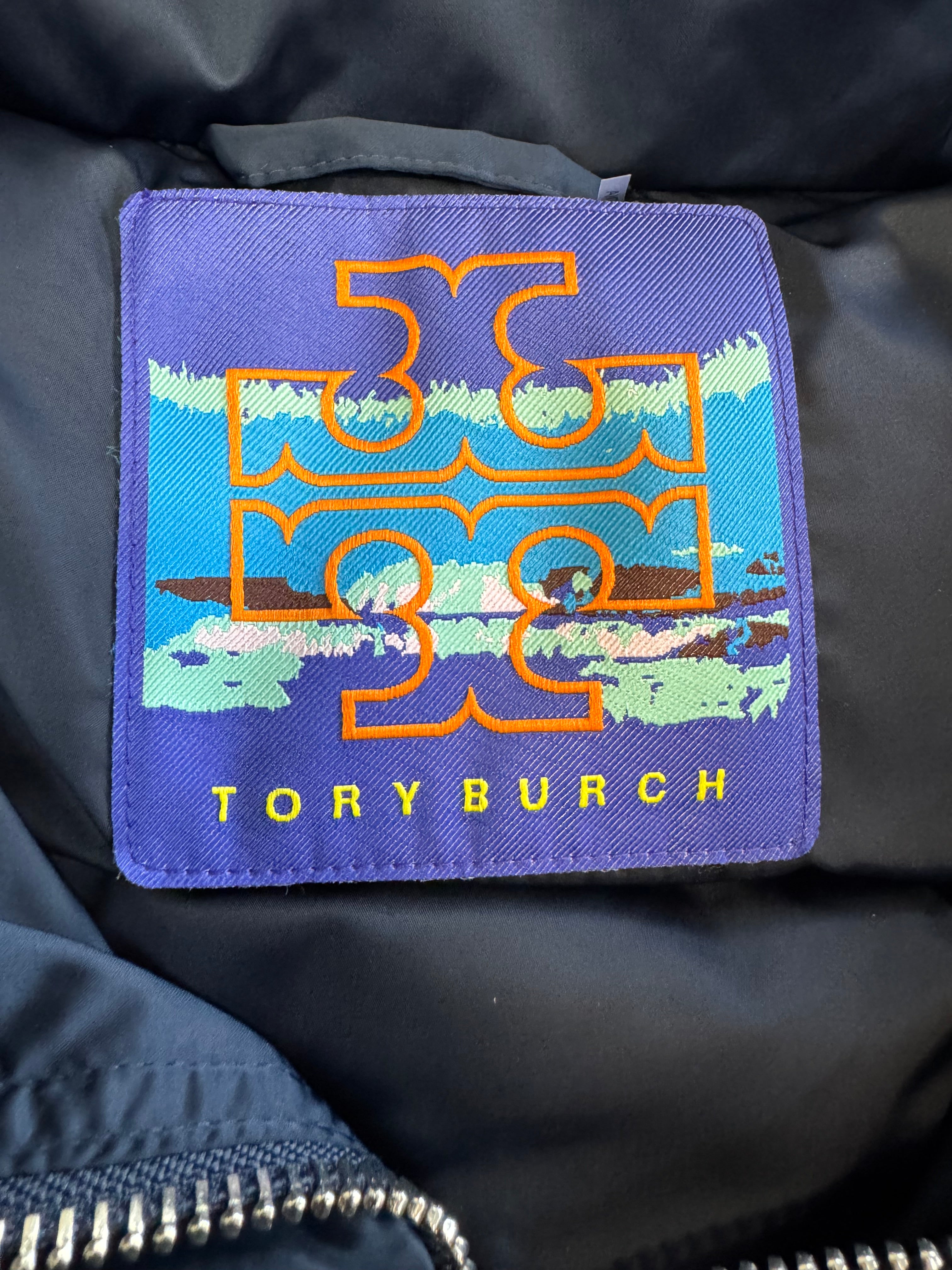 Embroidered patch with 'Tory Burch' logo on a dark fabric background