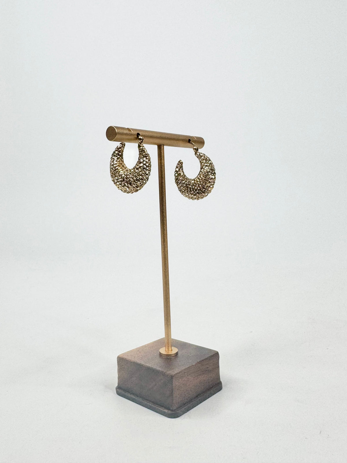 Pair of gold earrings on a wooden stand against a white background