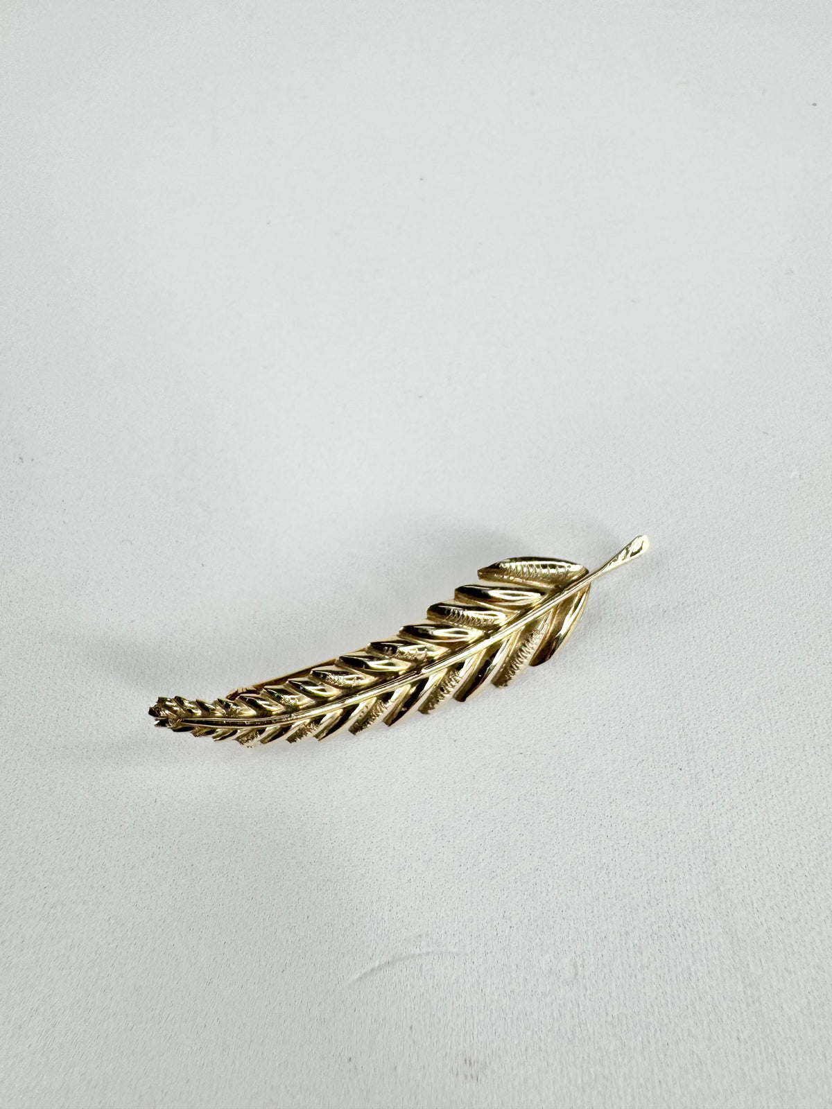 Gold feather-shaped brooch on a light gray background