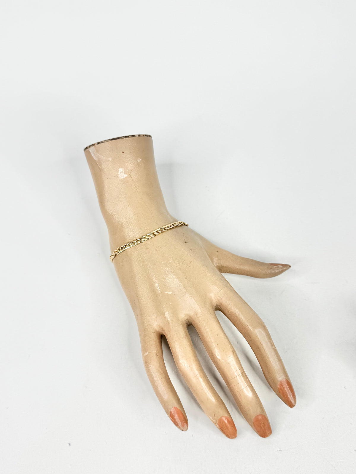 Mannequin hand wearing a gold bracelet on a white background