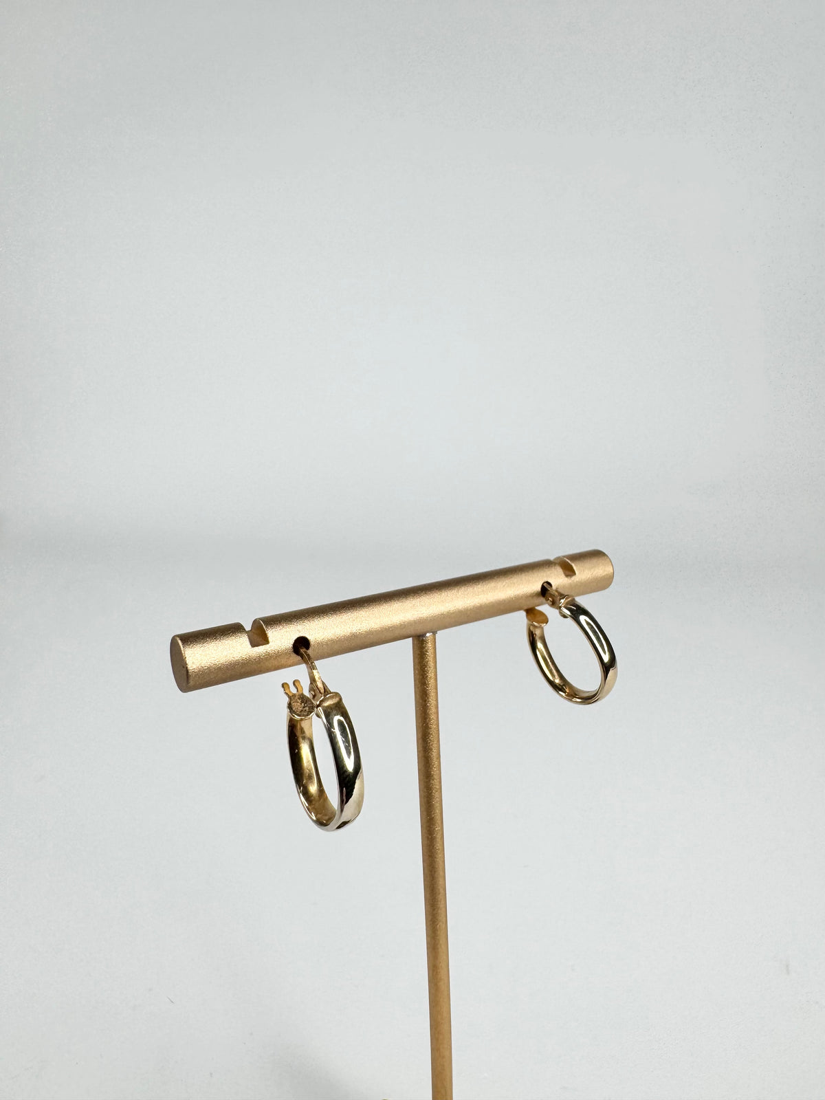 Gold hoop earrings on a gold earring stand against a light gray background