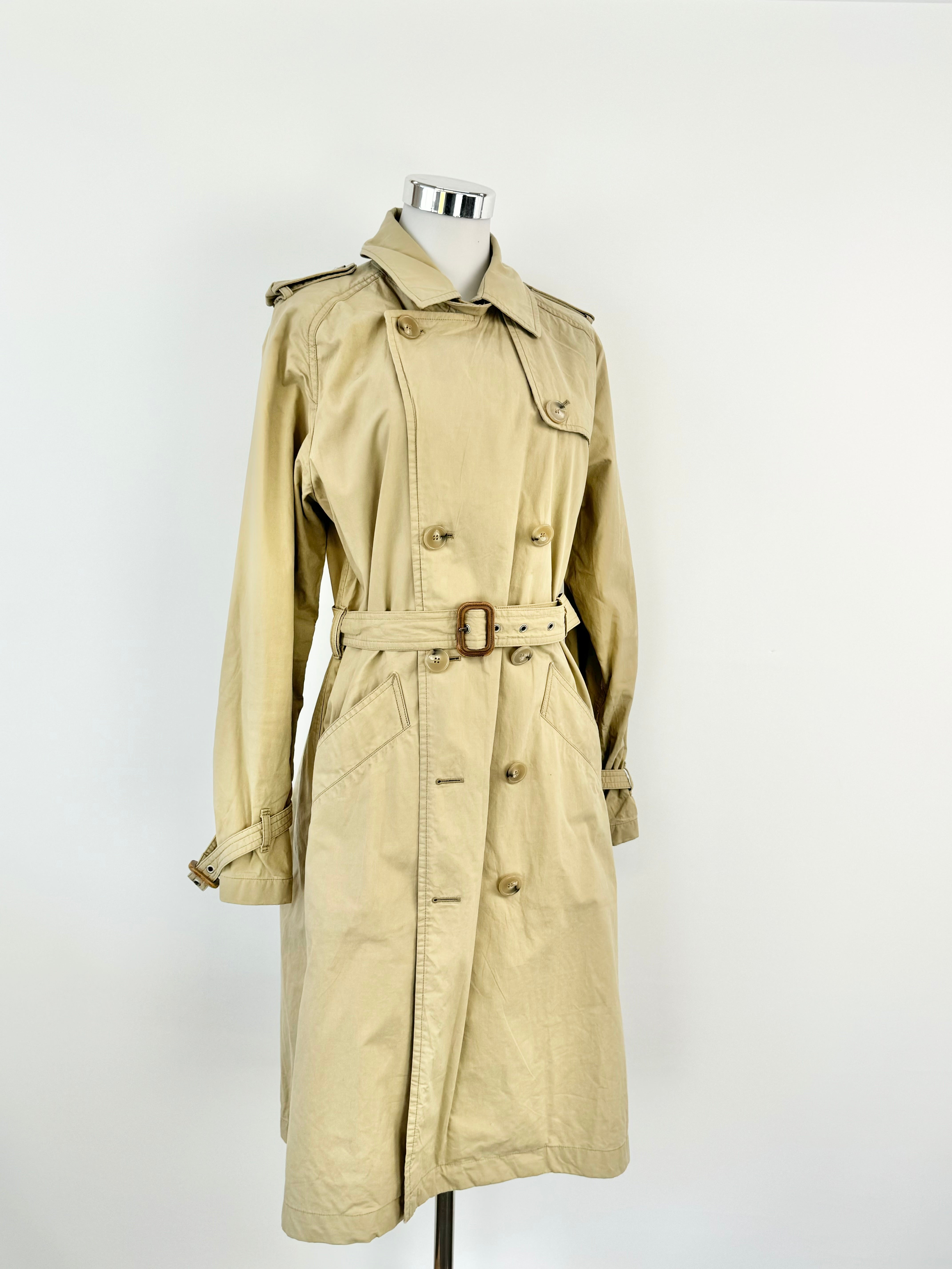 A beige trench coat with a belted waist and buttons down the front, displayed on a mannequin against a white background.