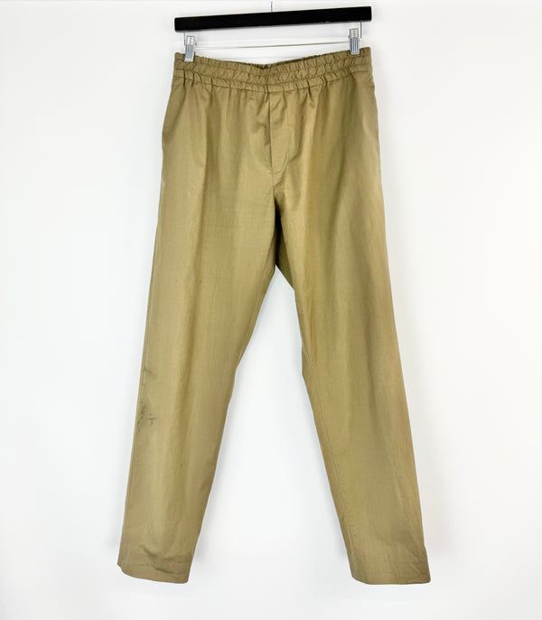 khaki pants hanging on a black rod against a white background