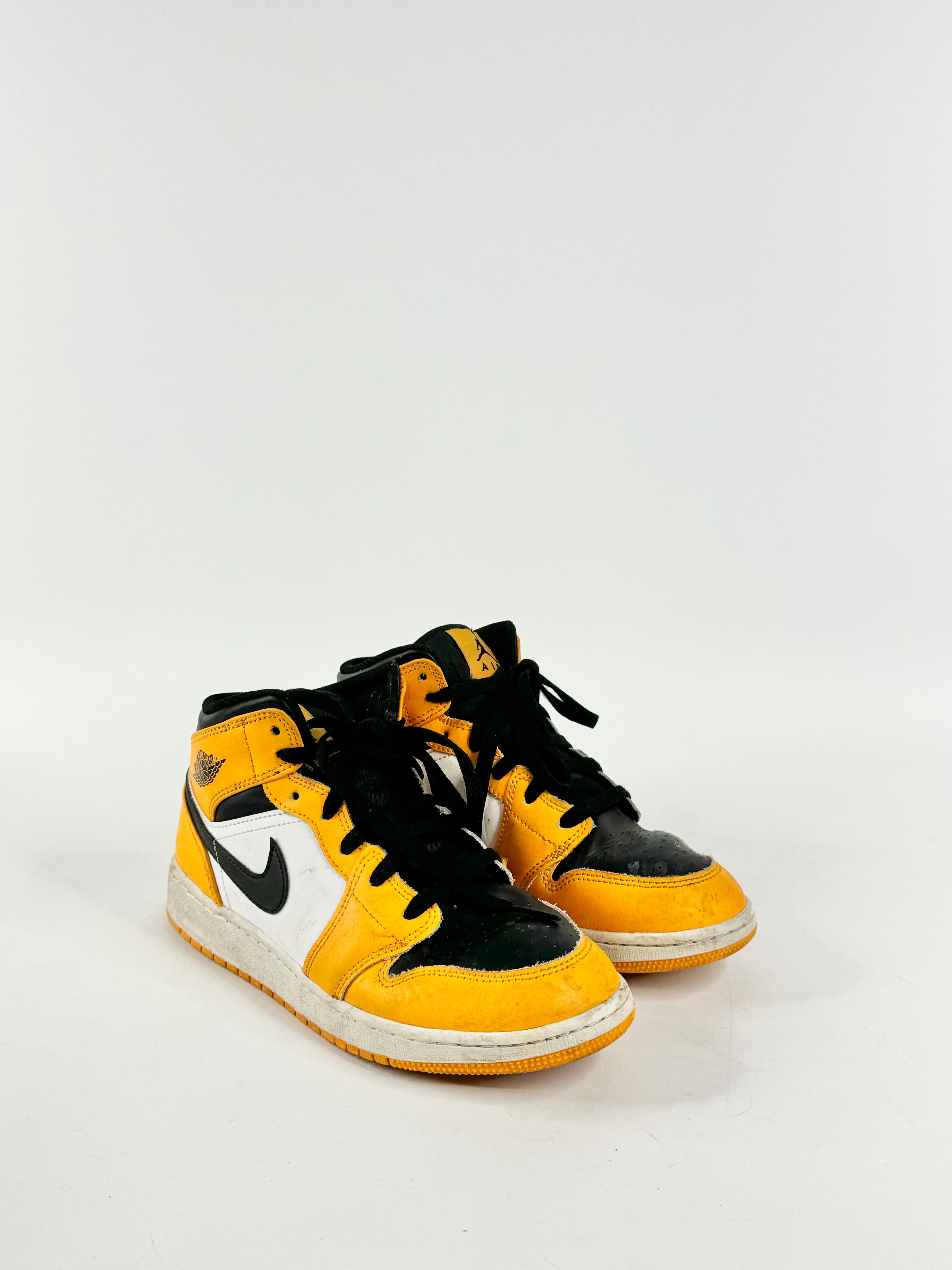 A pair of Air Jordan 1 Mid GS 'Reverse Kids' in buttery yellow, white, and black colors