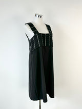 A black woolly apron dress on a mannequin, displaying signs of wear and a high neckline.