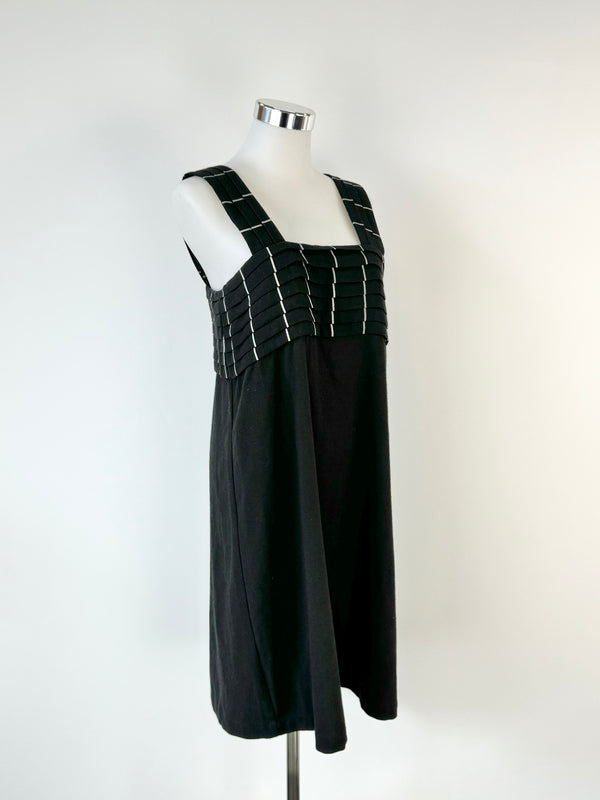 A black woolly apron dress on a mannequin, displaying signs of wear and a high neckline.