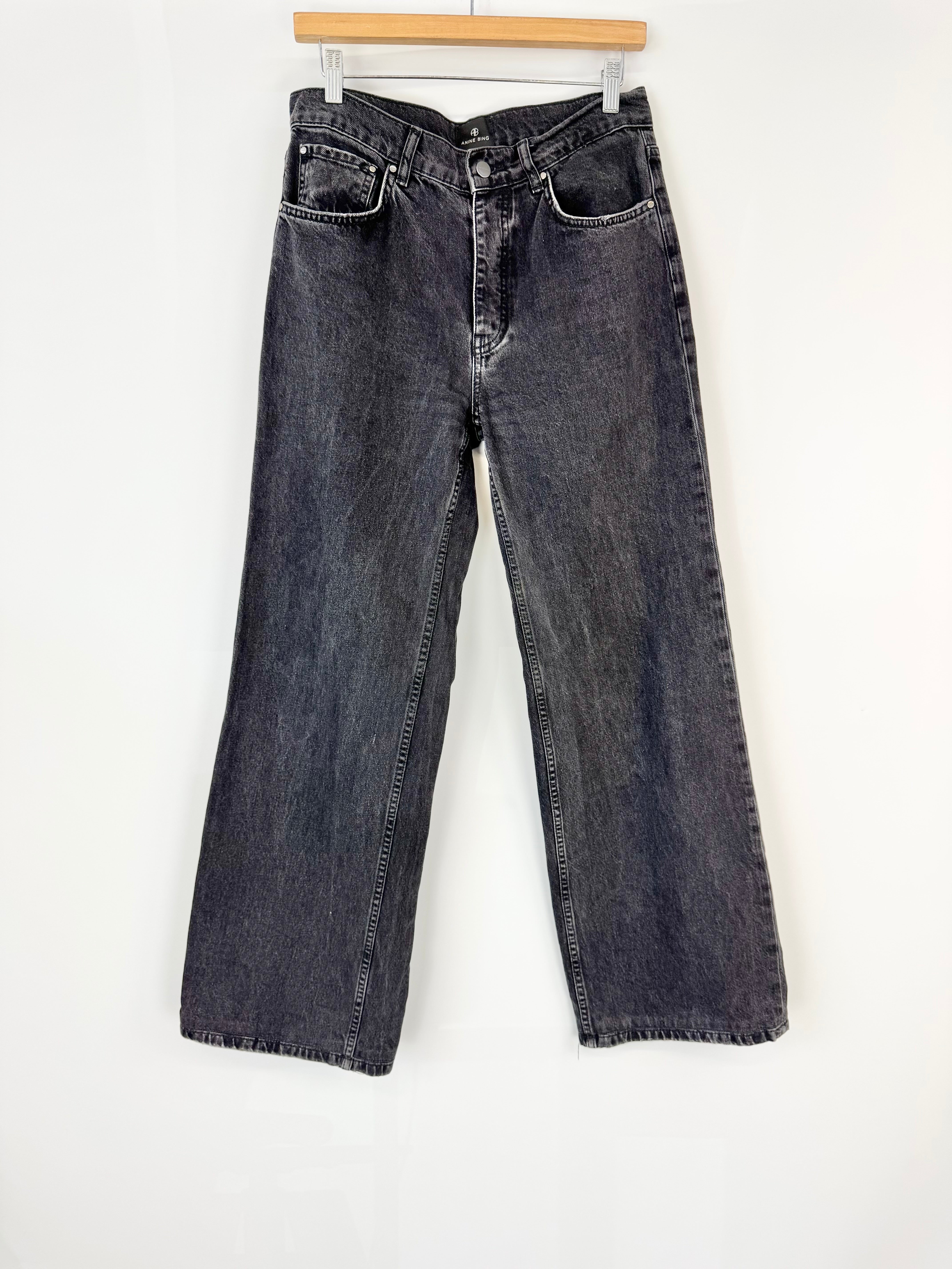 Pair of black jeans hanging on a wooden hanger against a white background