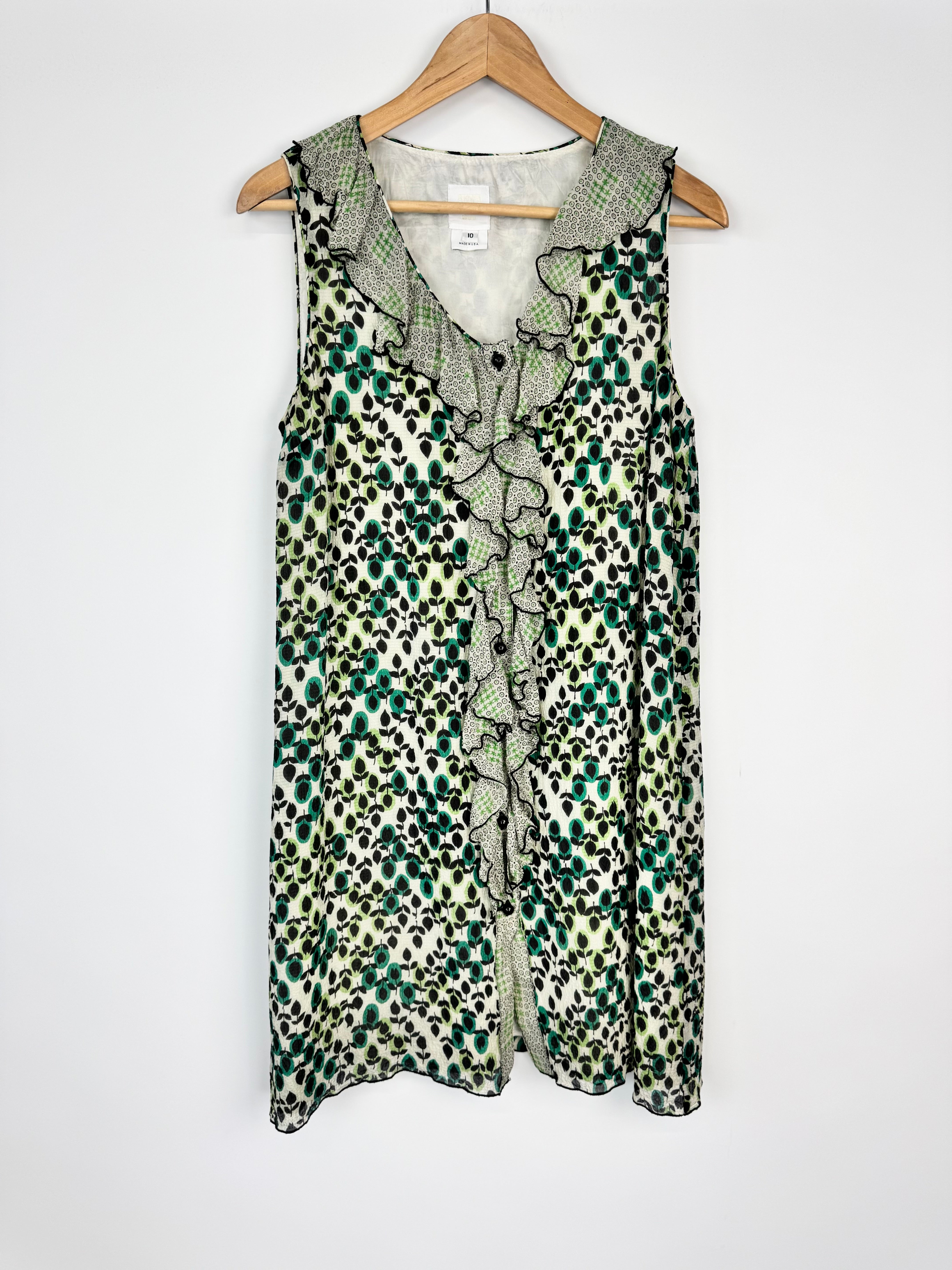 Green and white patterned sleeveless top on a wooden hanger against a white background