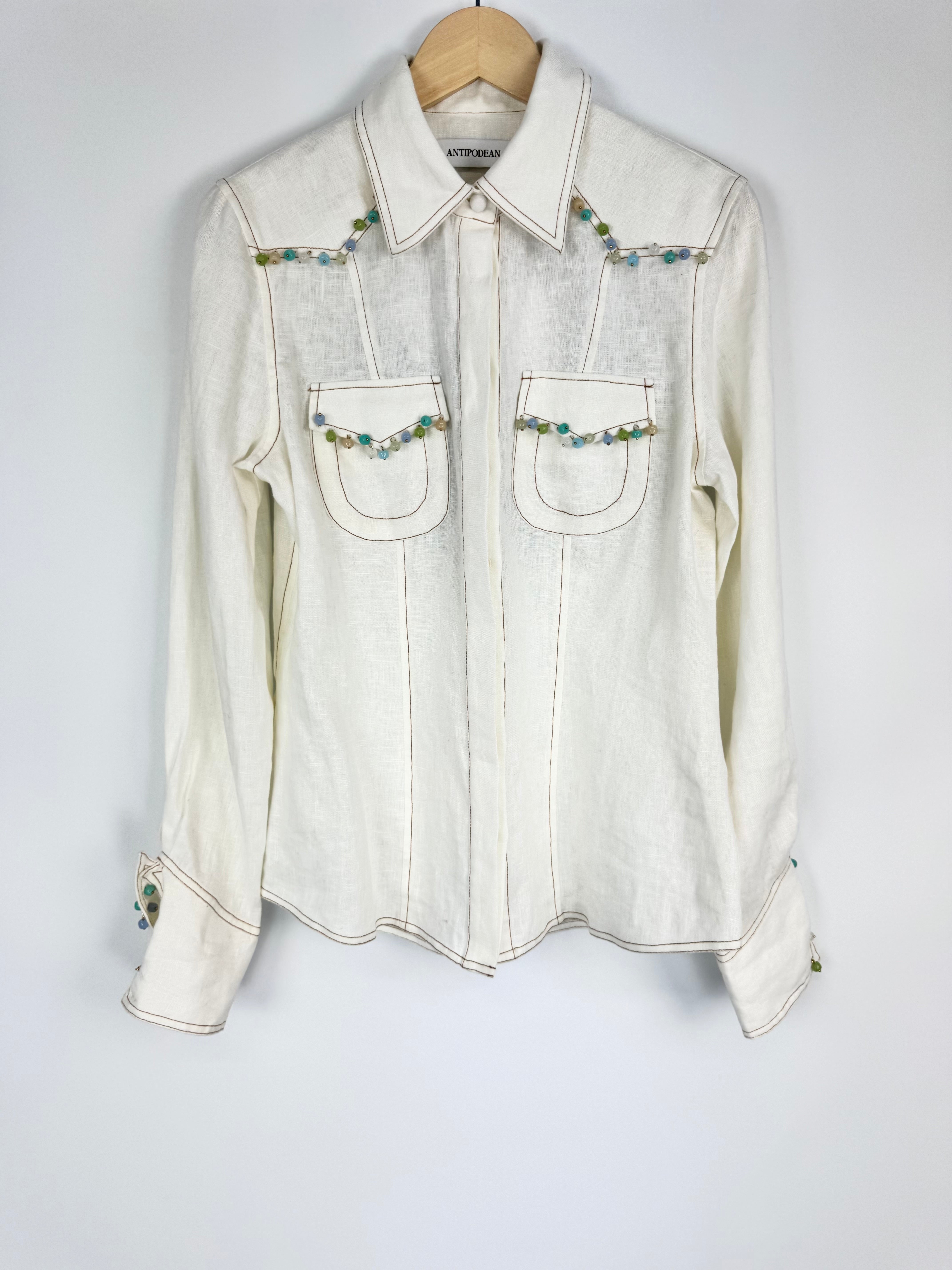 White denim shirt with bead embellishments on a hanger against a white background